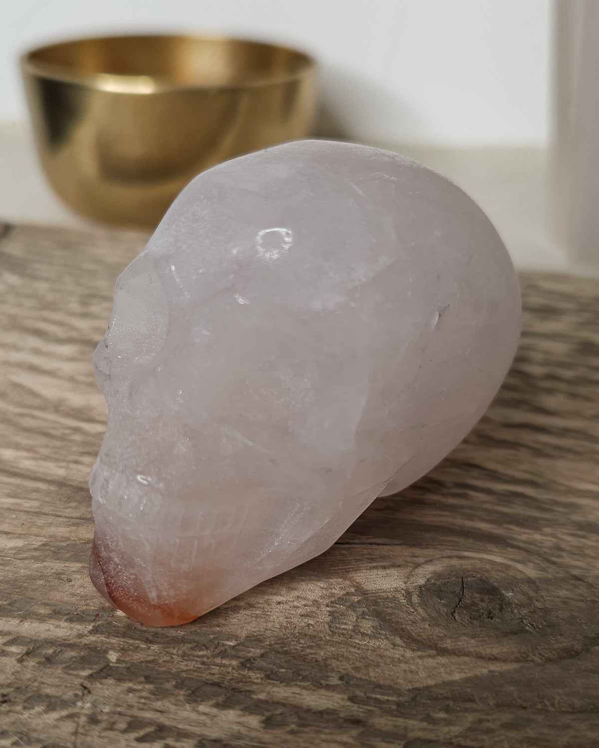 Rose Quartz crystal skull with natural red Hematite inclusions, showing soft pink tones and a reddish patch at the base.