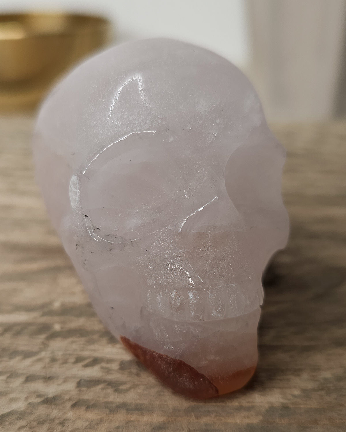 Rose Quartz crystal skull with natural red Hematite inclusions, showing soft pink tones and a reddish patch at the base