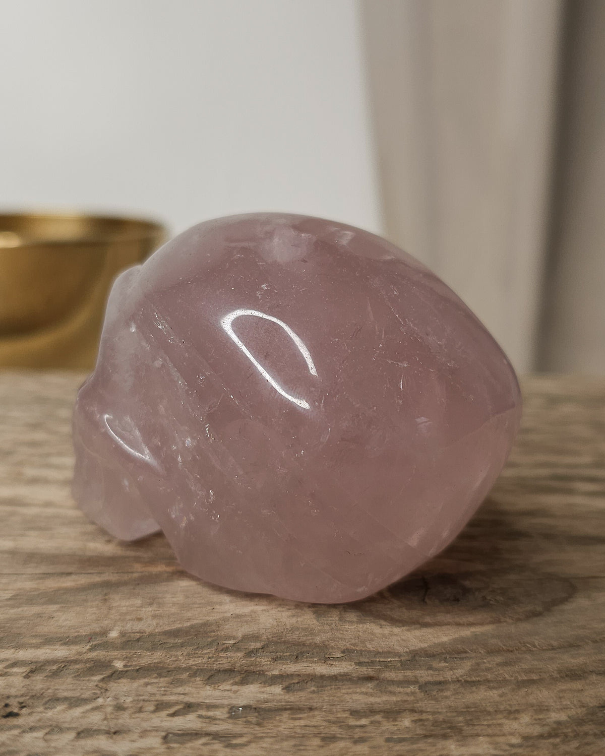 Rose Quartz crystal skull carving with soft pink tones and natural cloudy patterns, polished finish, displayed as a decorative crystal piece.