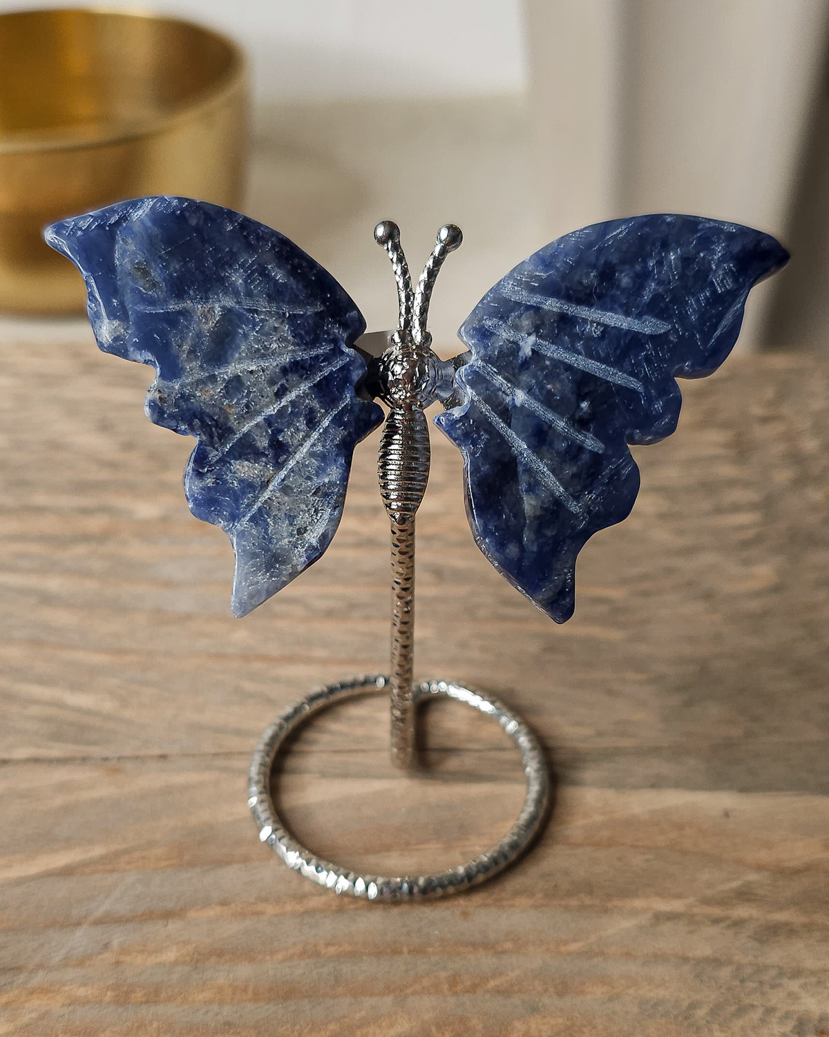 Sodalite butterfly carving on a silver-tone metal stand, featuring deep blue colouring with natural white veining.
