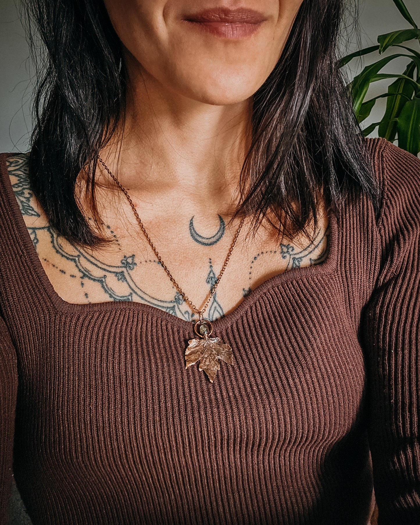 Close-up of a person wearing a brown ribbed sweater with a Copper electroformed Necklace with maple leaf pendant and golden rutilated Quartz crystal on a textured surface with leaves