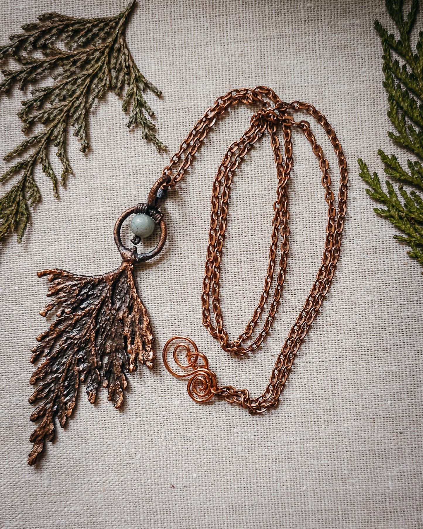 Handmade Copper electroformed Necklace with a cypress and Amazonite bead on a textured fabric background