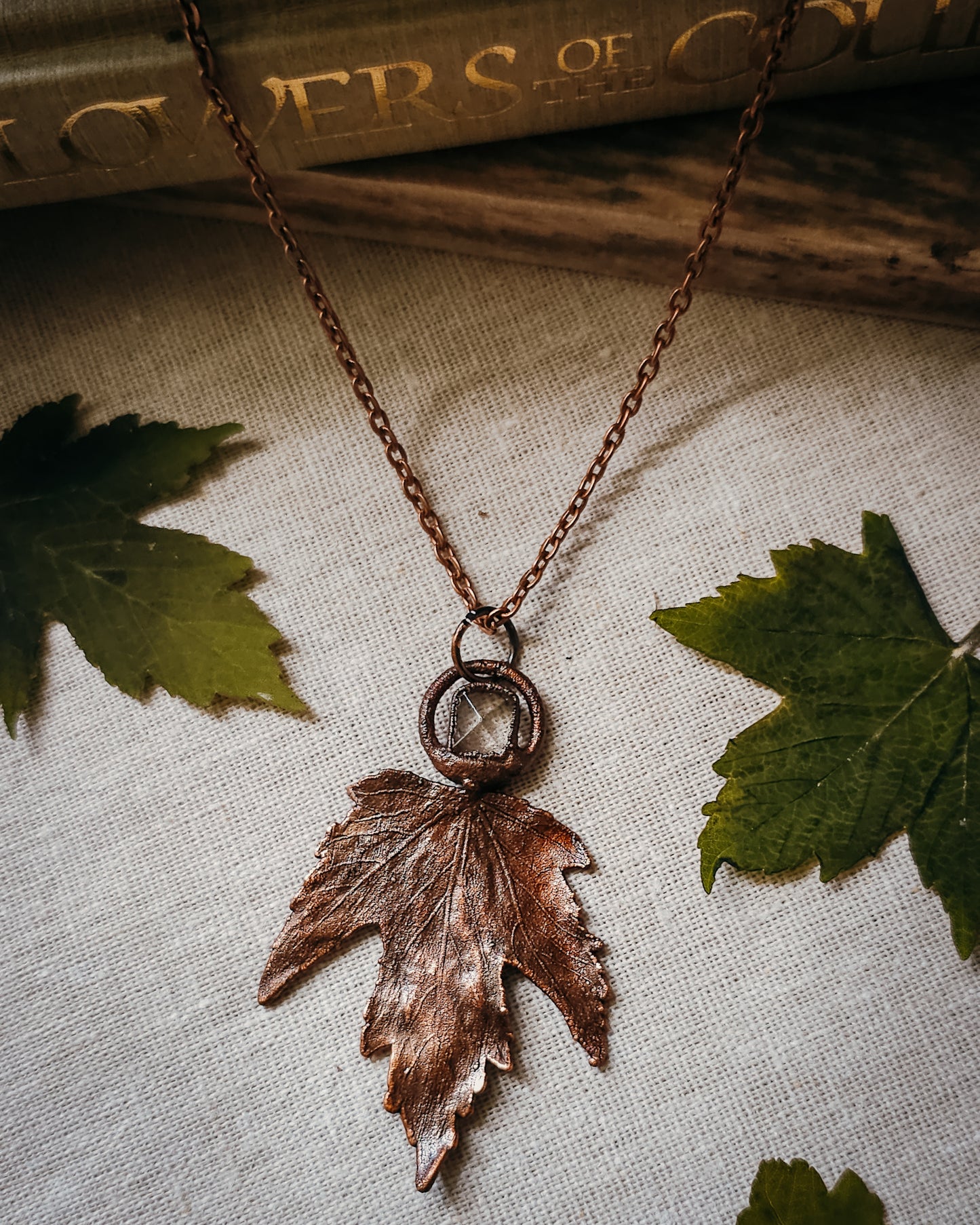Copper electroformed Necklace with maple leaf pendant and Quartz crystal on a textured surface with leaves