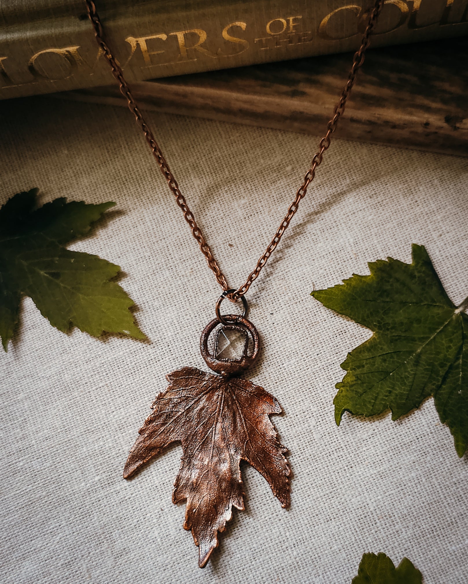 Copper electroformed Necklace with maple leaf pendant and Quartz crystal on a textured surface with leaves