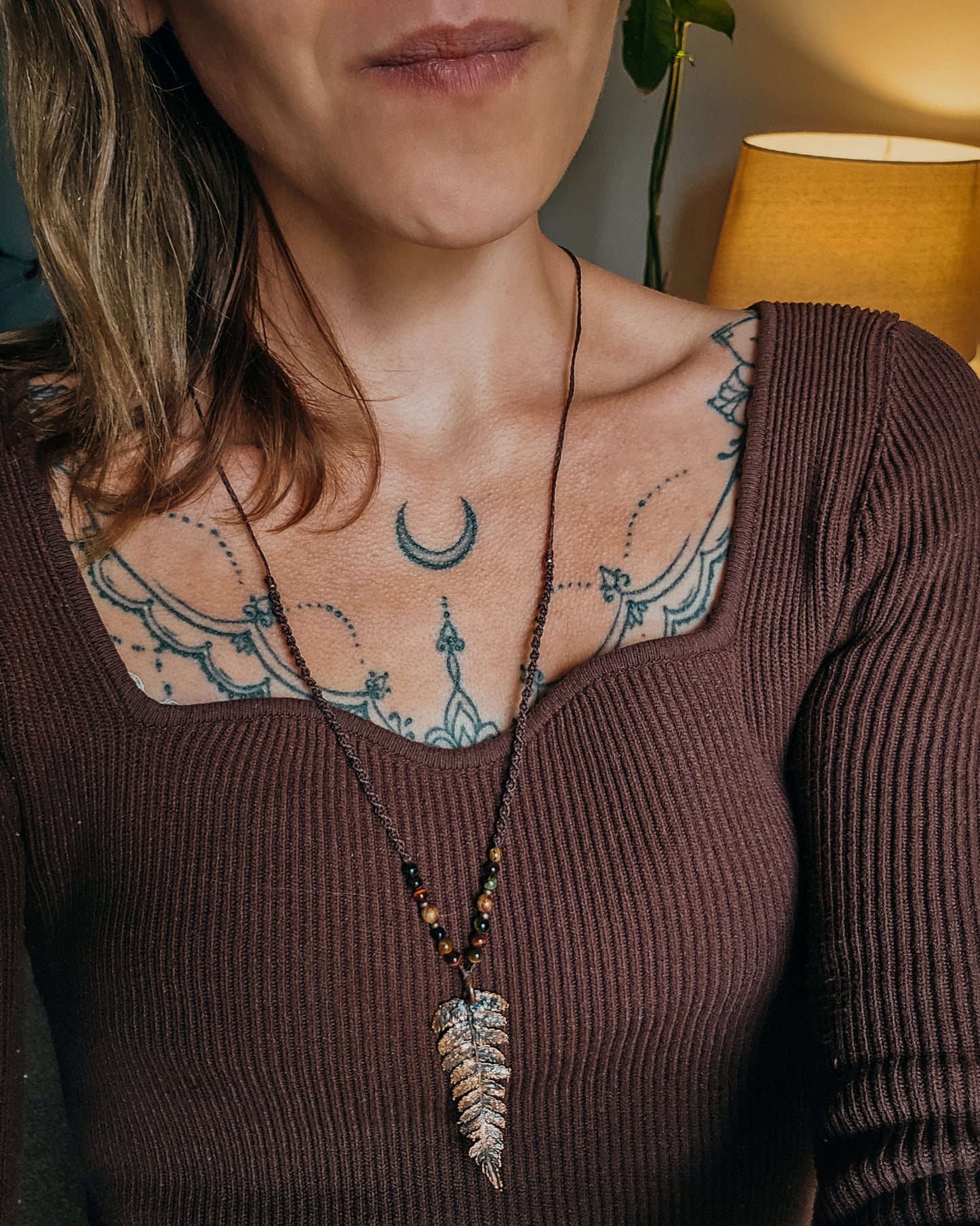 Close-up of a woman with tattoos on their shoulder and neck, wearing Necklace with tiger's eye and wooden beads and a copper electroformed fern charm. 