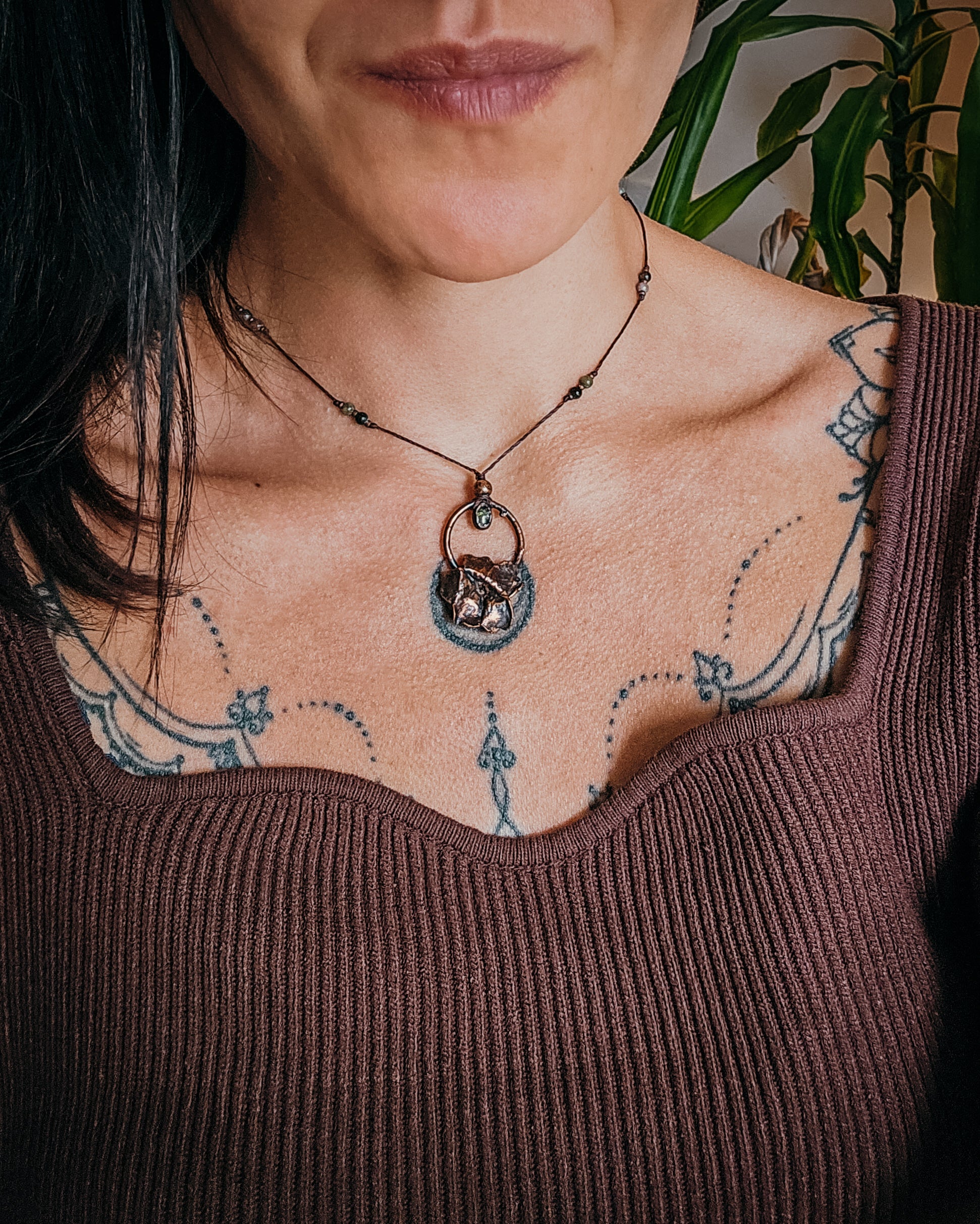 Handcrafted copper Primrose flower necklace worn on an adjustable cord, featuring a Green Tourmaline stone, green and pink Tourmaline beads, and intricate details. The real Scottish Primrose preserved in copper is shown worn against the neckline for scale.