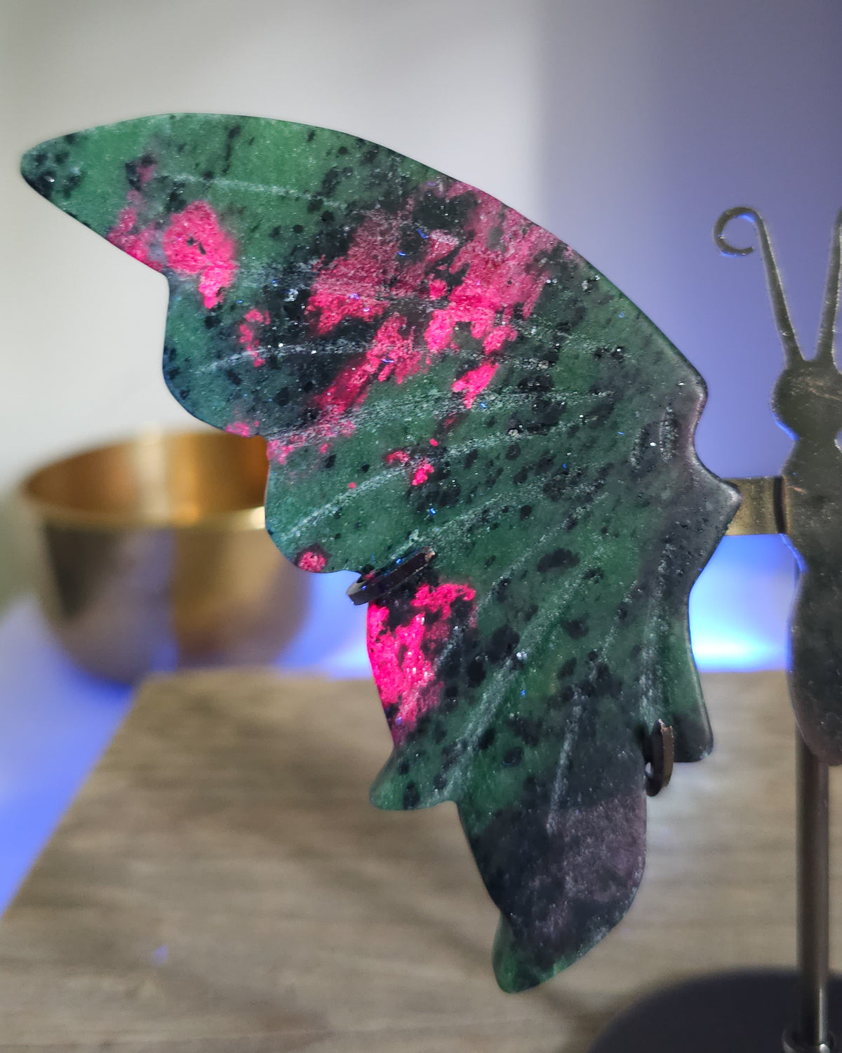Ruby in Zoisite butterfly wings with fluorescent Ruby inclusions on a black metal stand, glowing vivid pink-red under UV light.