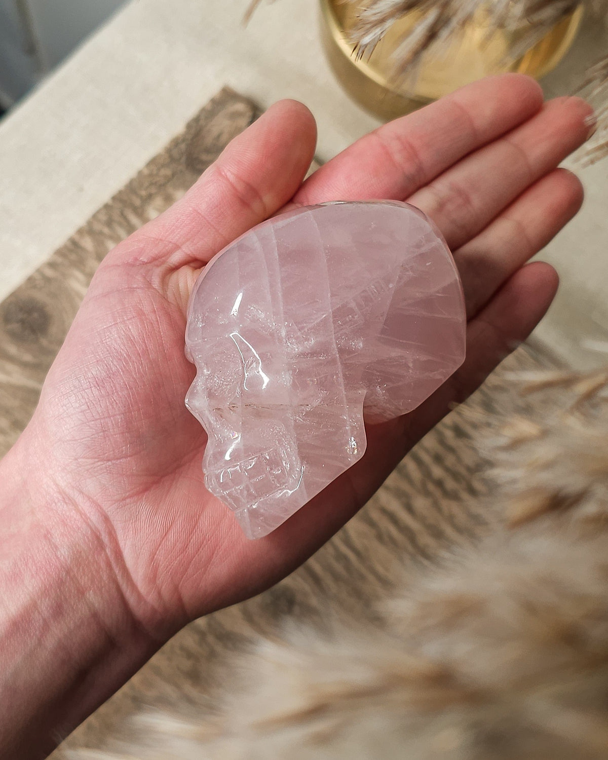 Rose Quartz crystal skull carving with soft pink tones and natural cloudy patterns, polished finish, displayed as a decorative crystal piece.