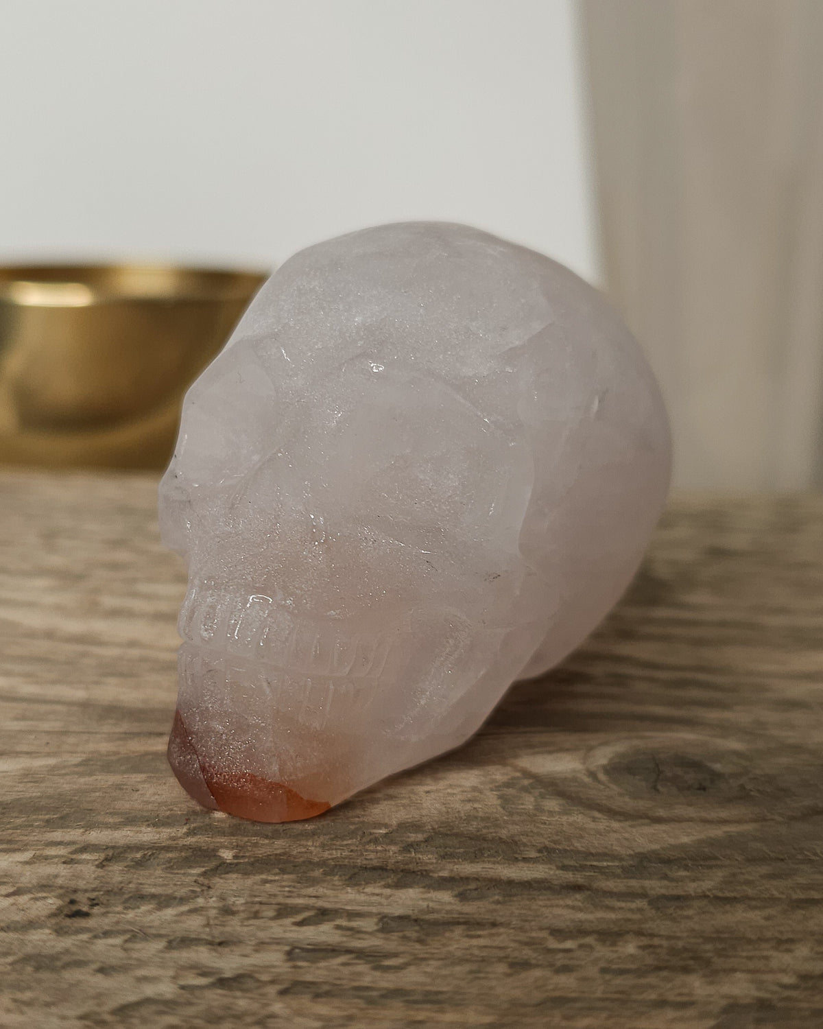 Rose Quartz crystal skull with natural red Hematite inclusions, showing soft pink tones and a reddish patch at the base.