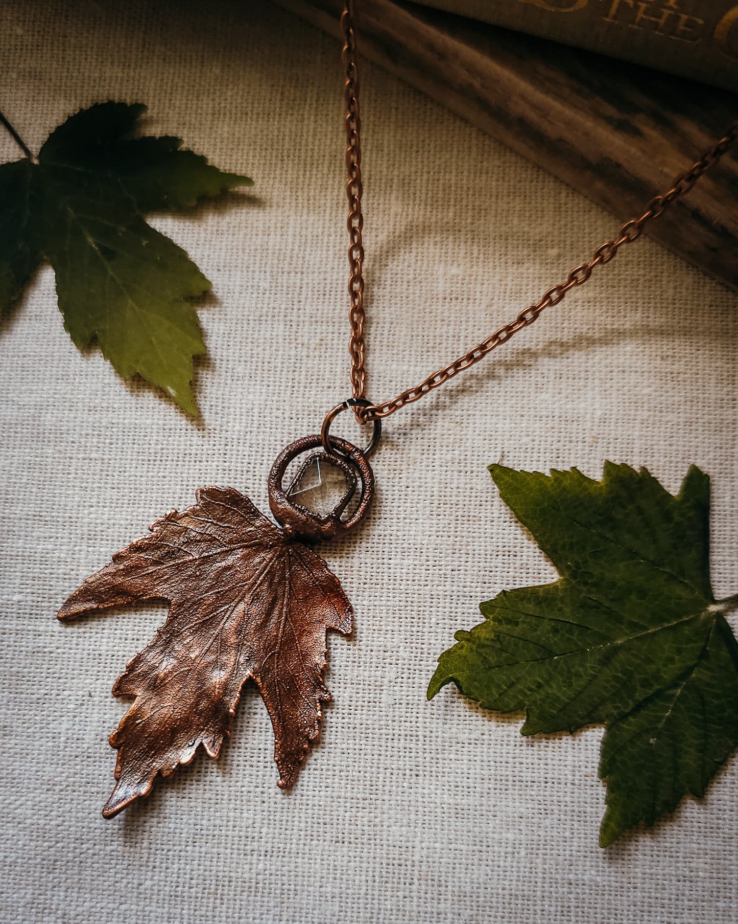 Copper electroformed Necklace with maple leaf pendant and Quartz crystal on a textured surface with leaves