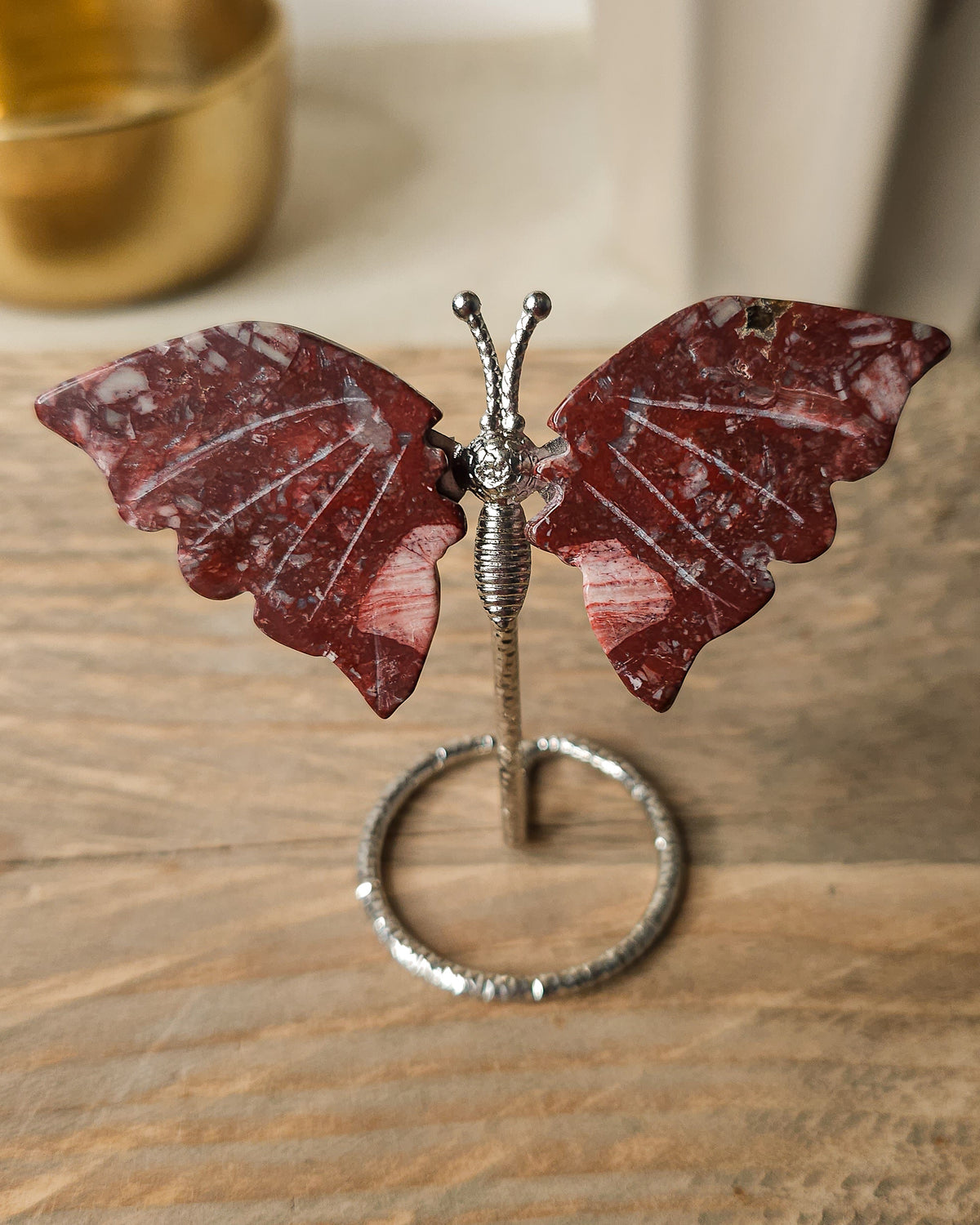 Red Jasper butterfly carving on a silver-tone metal stand, featuring deep brick-red colouring and natural white mineral patterns.
