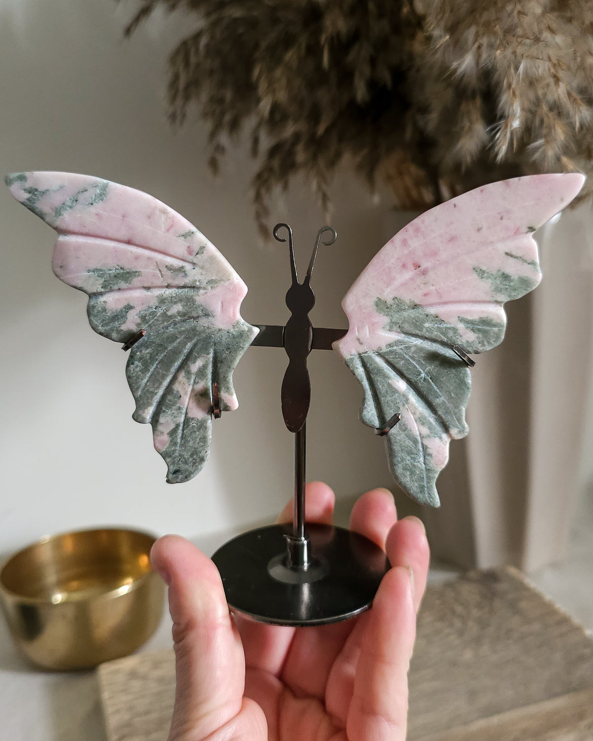 Pink Opal butterfly wings carved from natural pink opal, displayed on a black metal stand, showing soft pink and creamy tones.