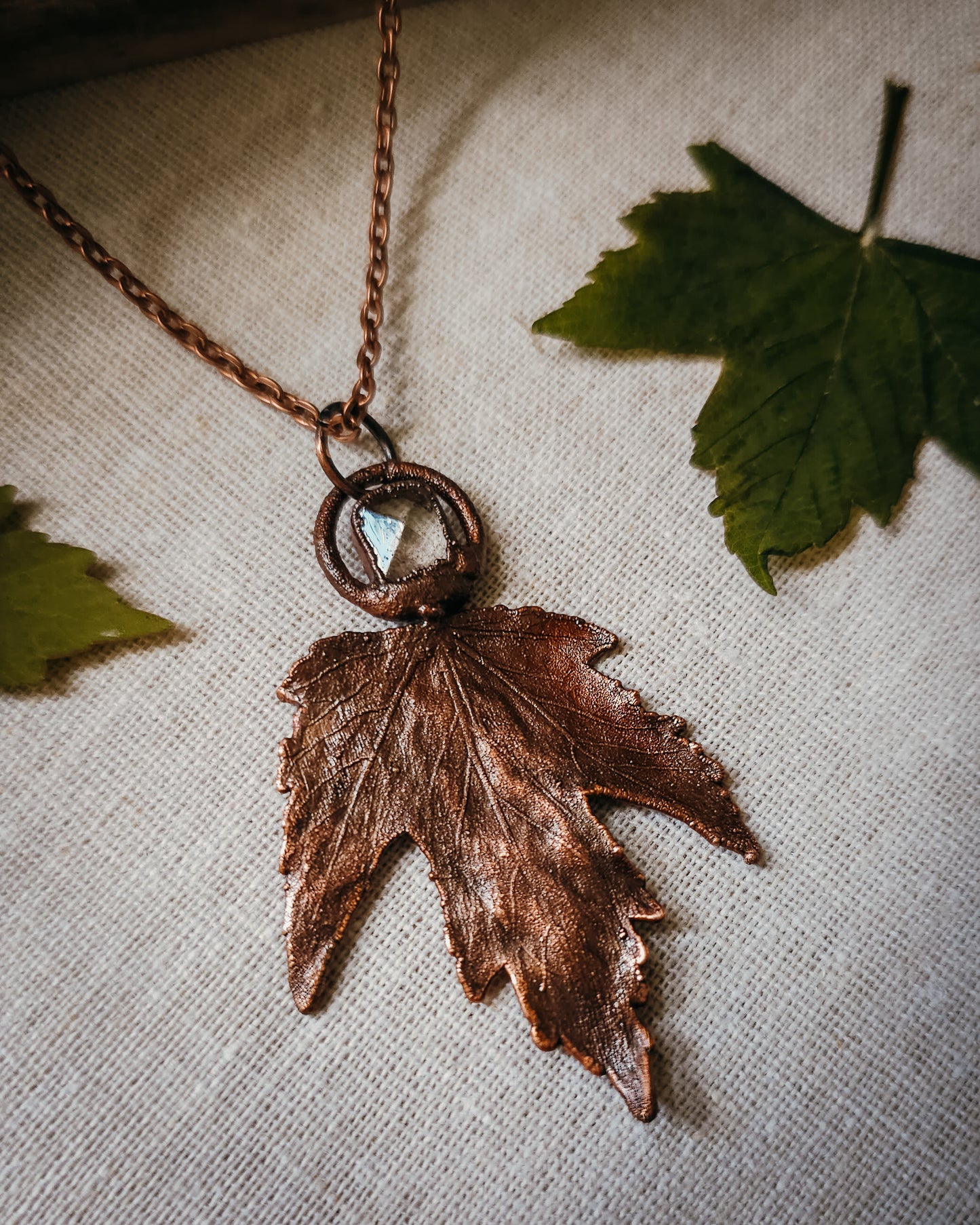 Copper electroformed Necklace with maple leaf pendant and Quartz crystal on a textured surface with leaves