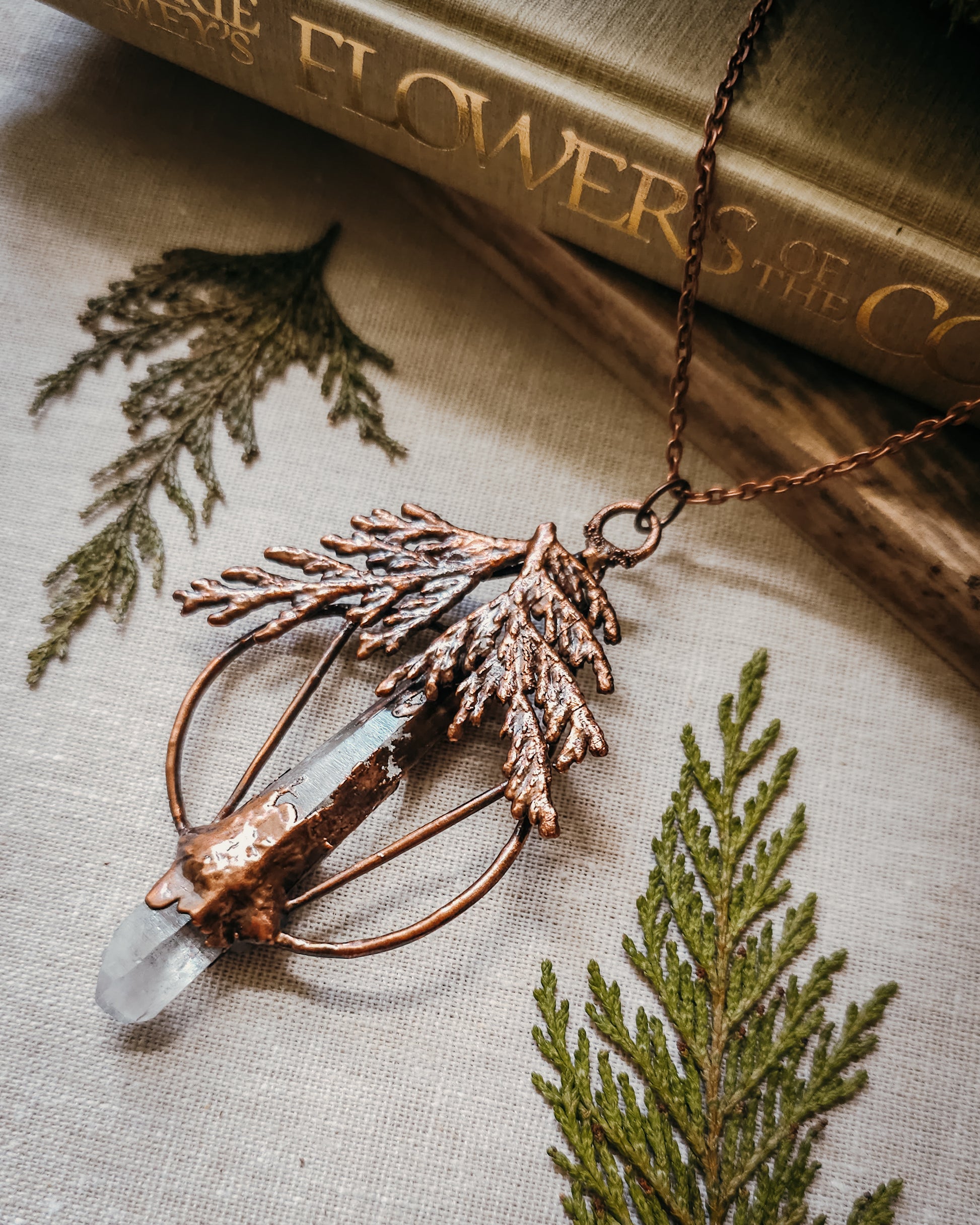 Handmade Copper electroformed Necklace with a cypress and clear Quartz crystal pendant on a textured fabric background