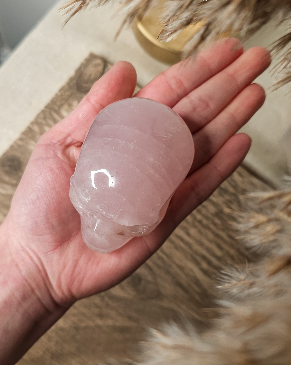 Rose Quartz crystal skull carving with soft pink tones and natural cloudy patterns, polished finish, displayed as a decorative crystal piece.