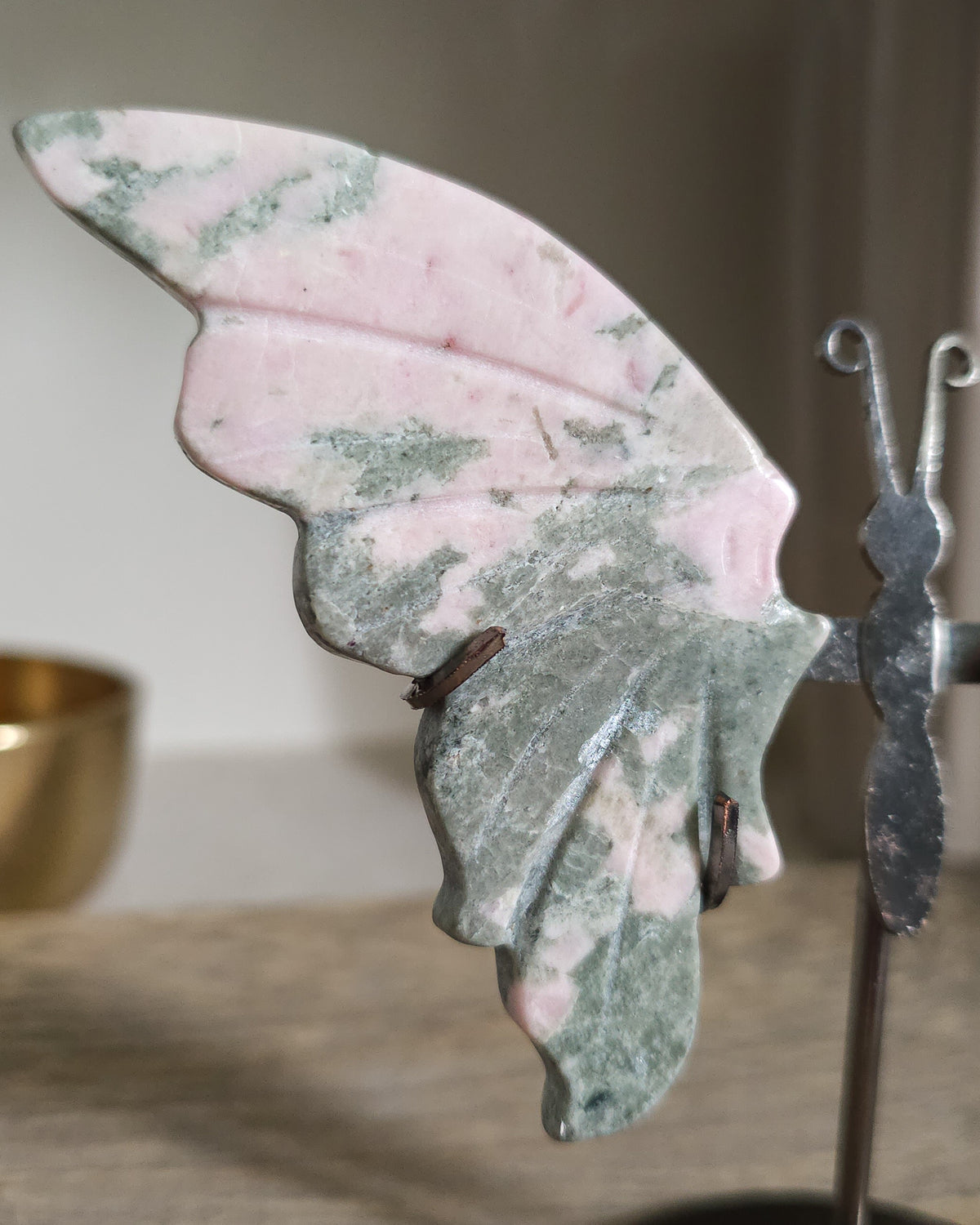 Pink Opal butterfly wings carved from natural pink opal, displayed on a black metal stand, showing soft pink and creamy tones.