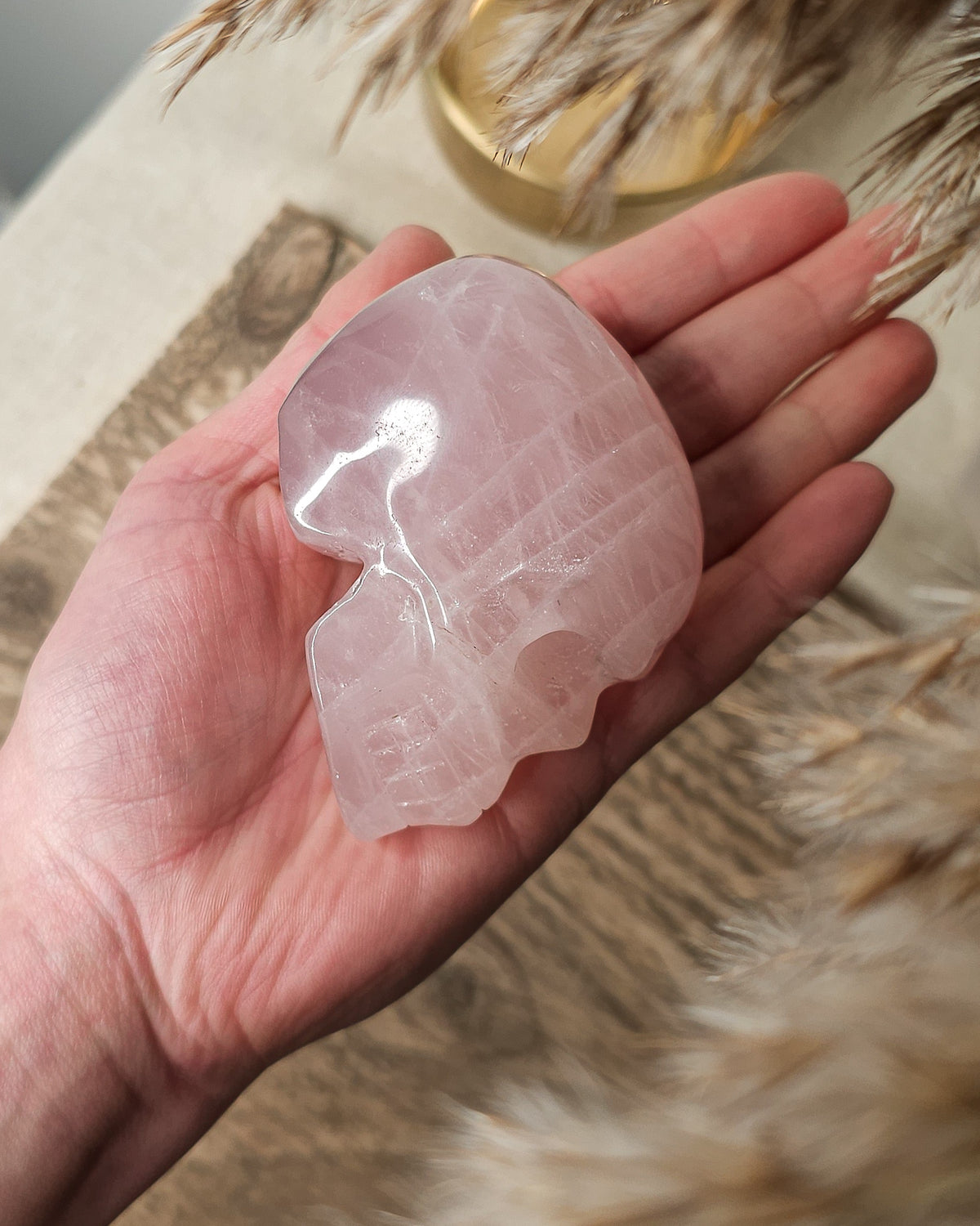 Rose Quartz crystal skull carving with soft pink tones and natural cloudy patterns, polished finish, displayed as a decorative crystal piece.