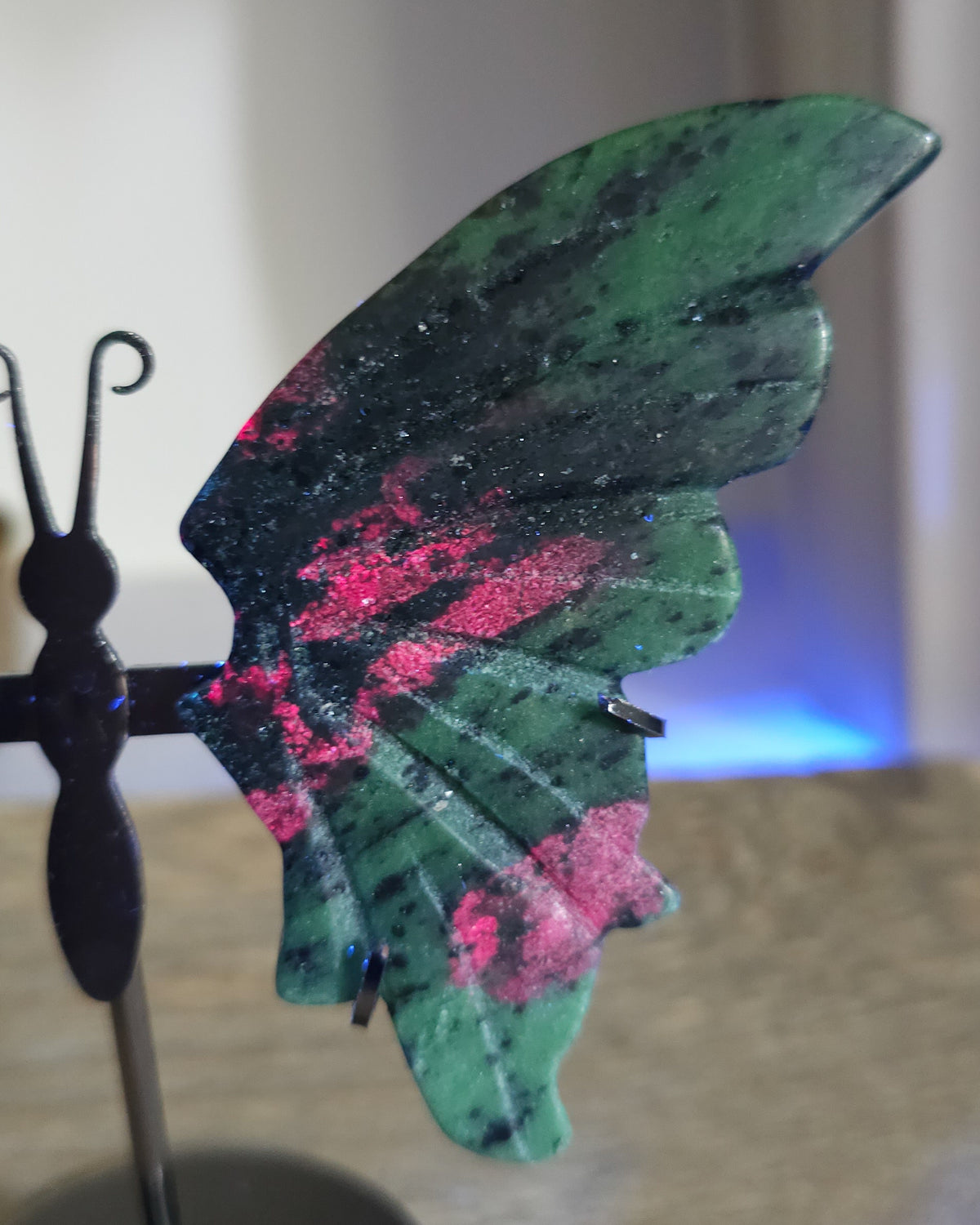 Ruby in Zoisite butterfly wings with fluorescent Ruby inclusions on a black metal stand, glowing vivid pink-red under UV light.
