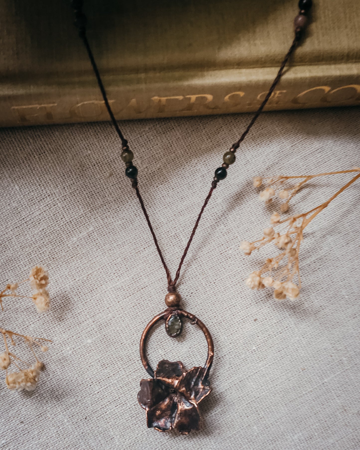 Handcrafted copper electroformed Primrose flower necklace featuring a natural Green Tourmaline stone, green and pink Tourmaline beads, brass accent beads on an adjustable cord. Created from a real Primrose flower gathered in Scotland and inspired by woodland folklore, renewal, and the magic of hidden pathways.