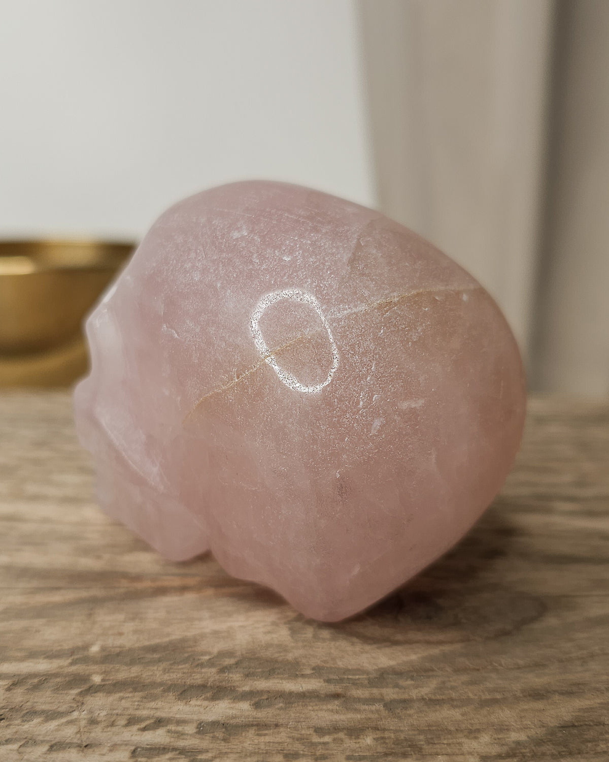 Rose Quartz crystal skull with natural red Hematite inclusions, showing soft pink tones and a reddish patch at the back.