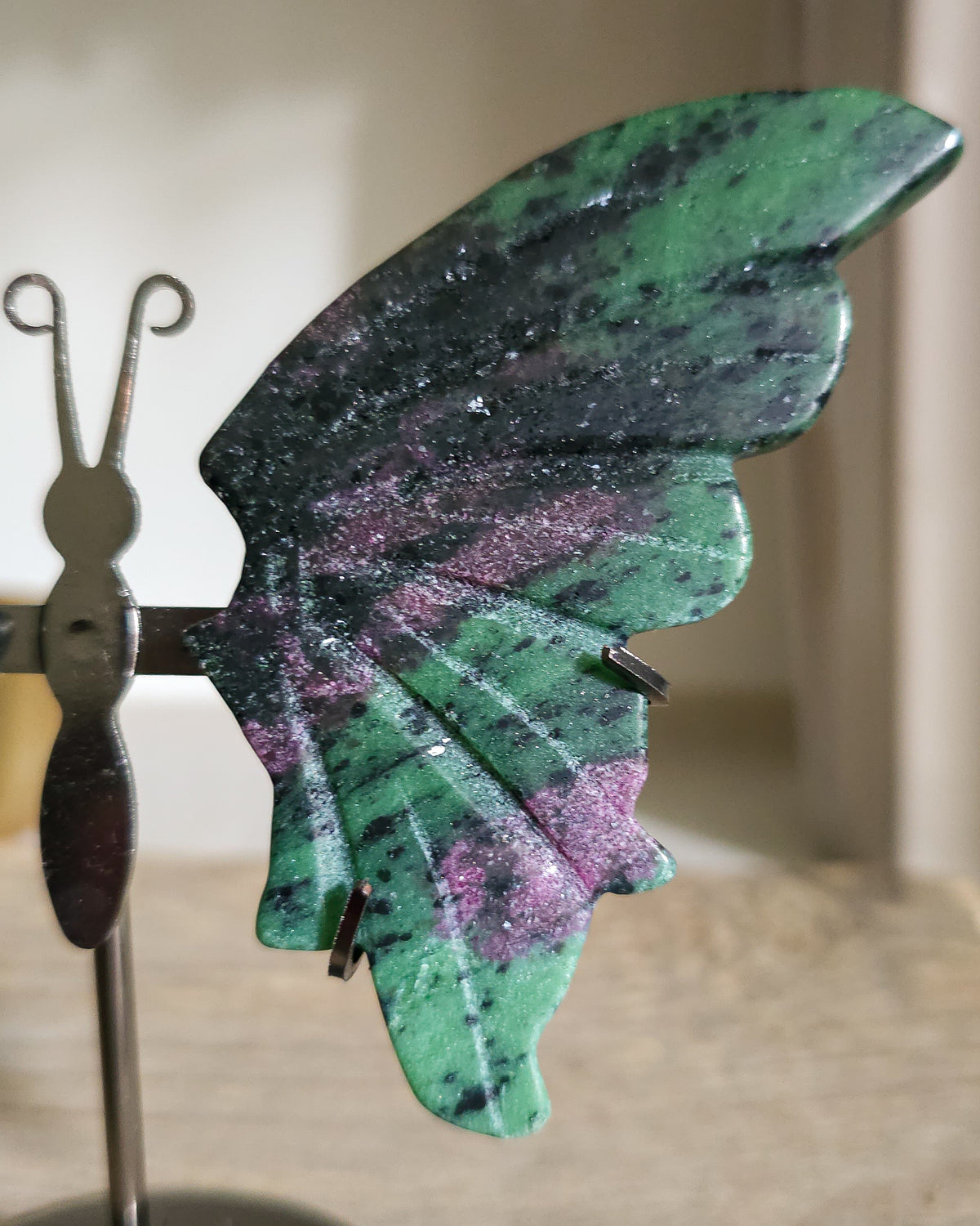 Ruby in Zoisite butterfly wings with fluorescent Ruby inclusions on a black metal stand, glowing vivid pink-red under UV light.. 