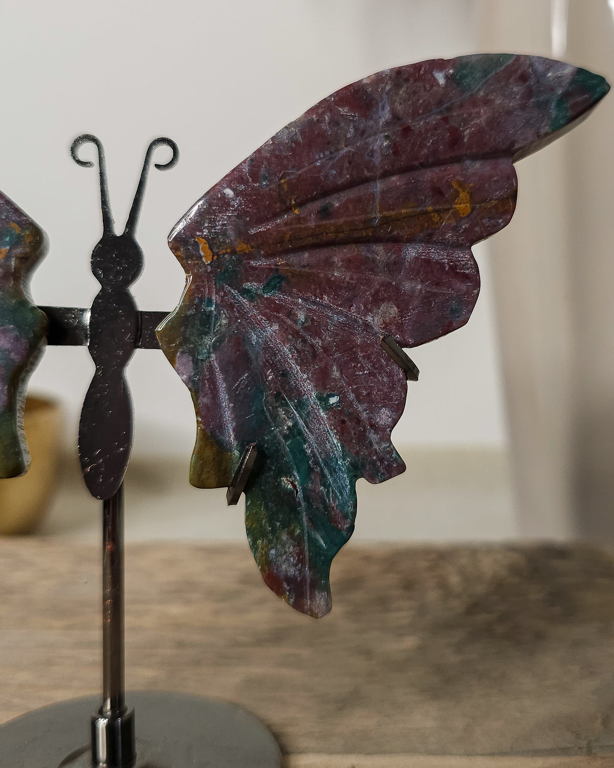 Jasper butterfly wings on a black metal stand, featuring earthy burgundy, green and golden natural patterns.. 