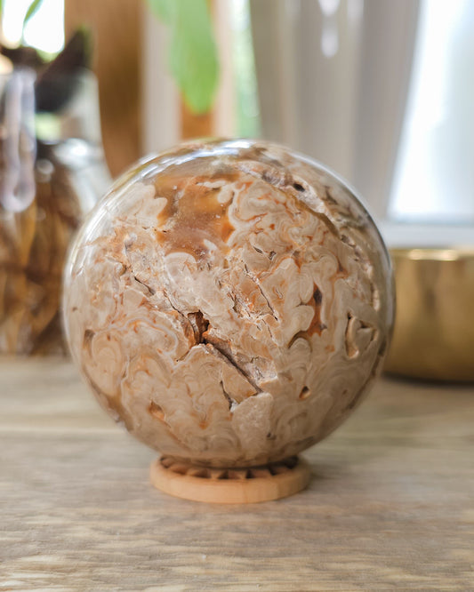 Chocolate Calcite sphere with natural druzy crystal cavities, orbicular banding and warm caramel, cream and brown patterns, displayed on a wooden stand.