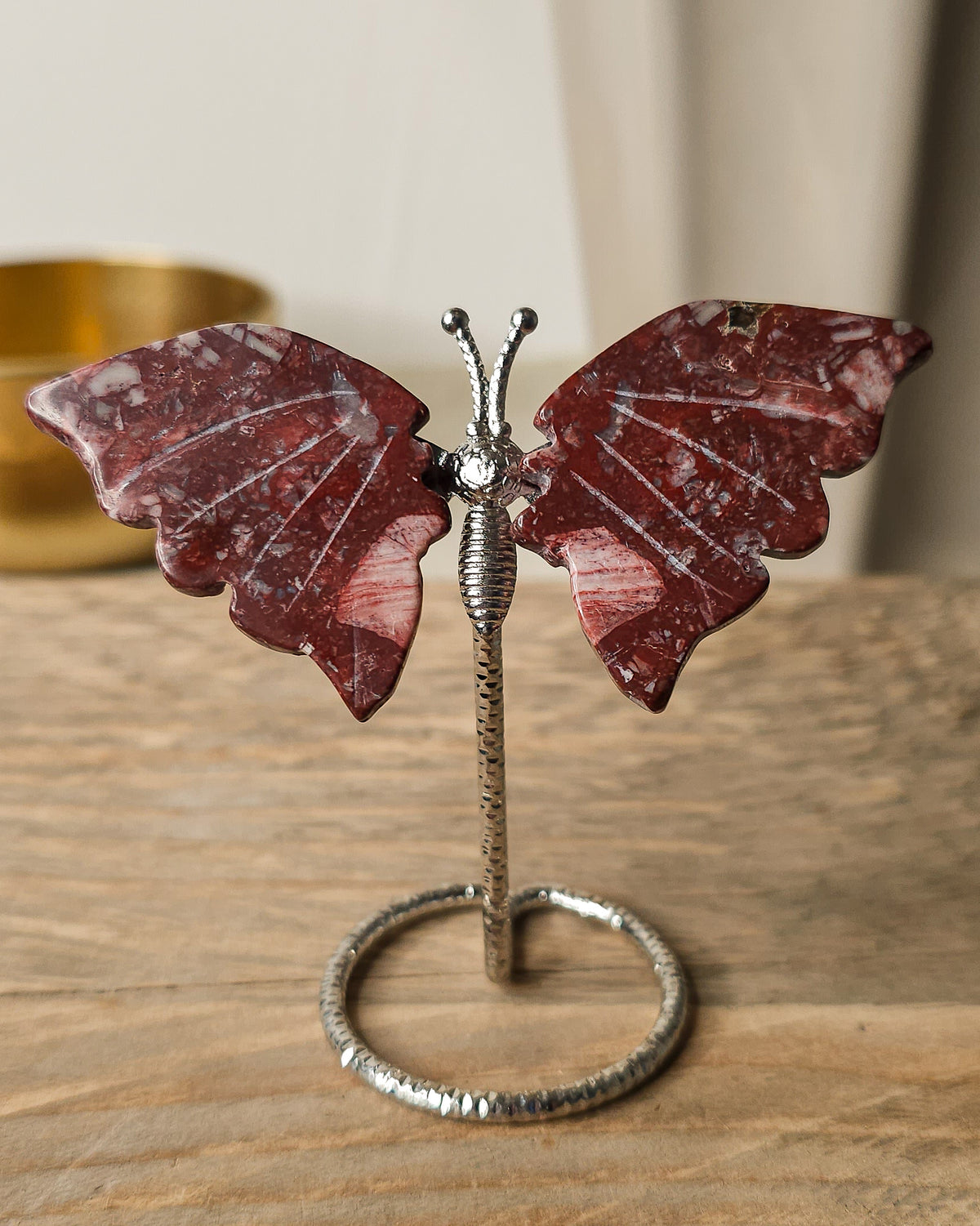 Red Jasper butterfly carving on a silver-tone metal stand, featuring deep brick-red colouring and natural white mineral patterns.

