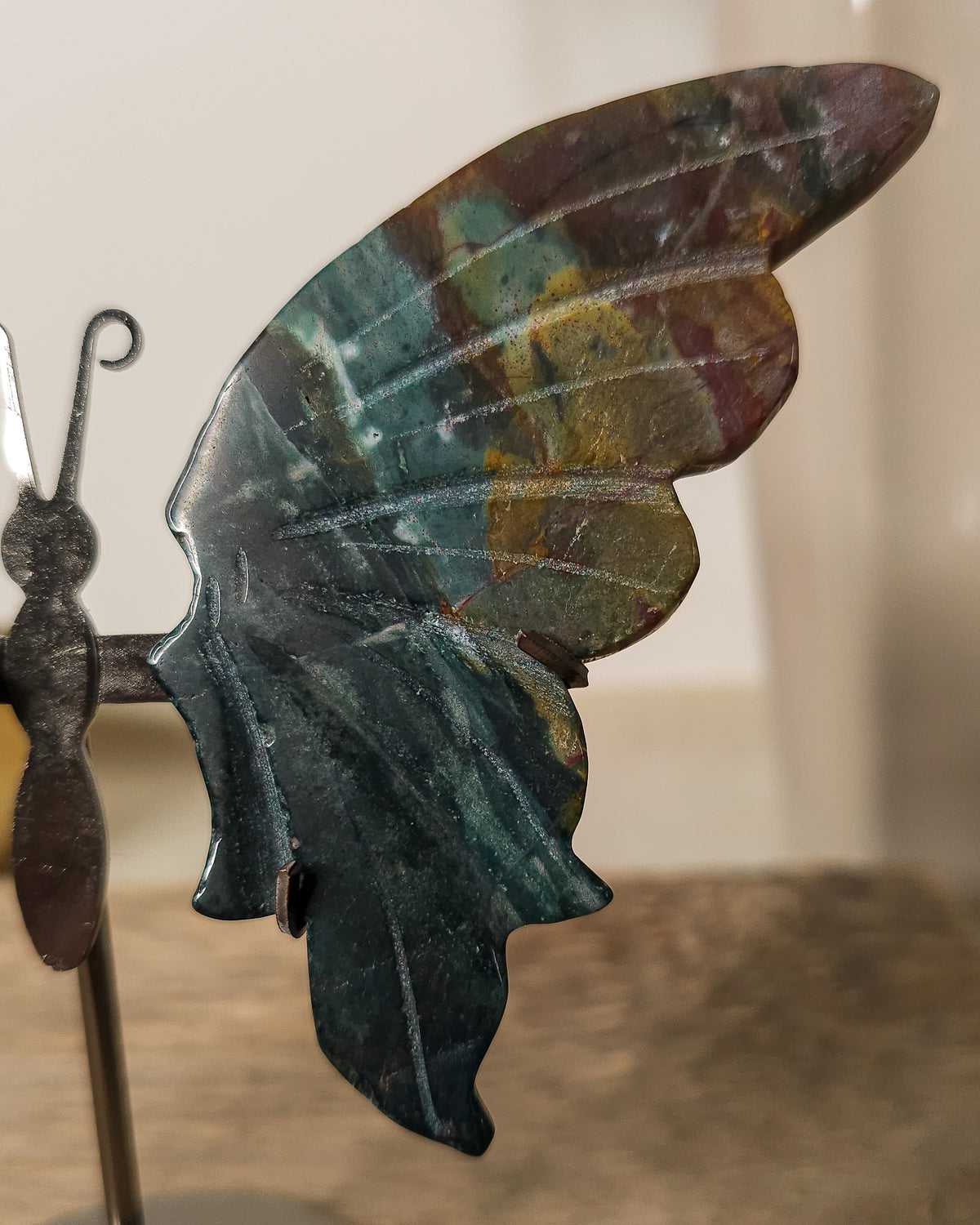 Jasper butterfly wings on a black metal stand, featuring deep green, earthy brown and golden natural patterns.