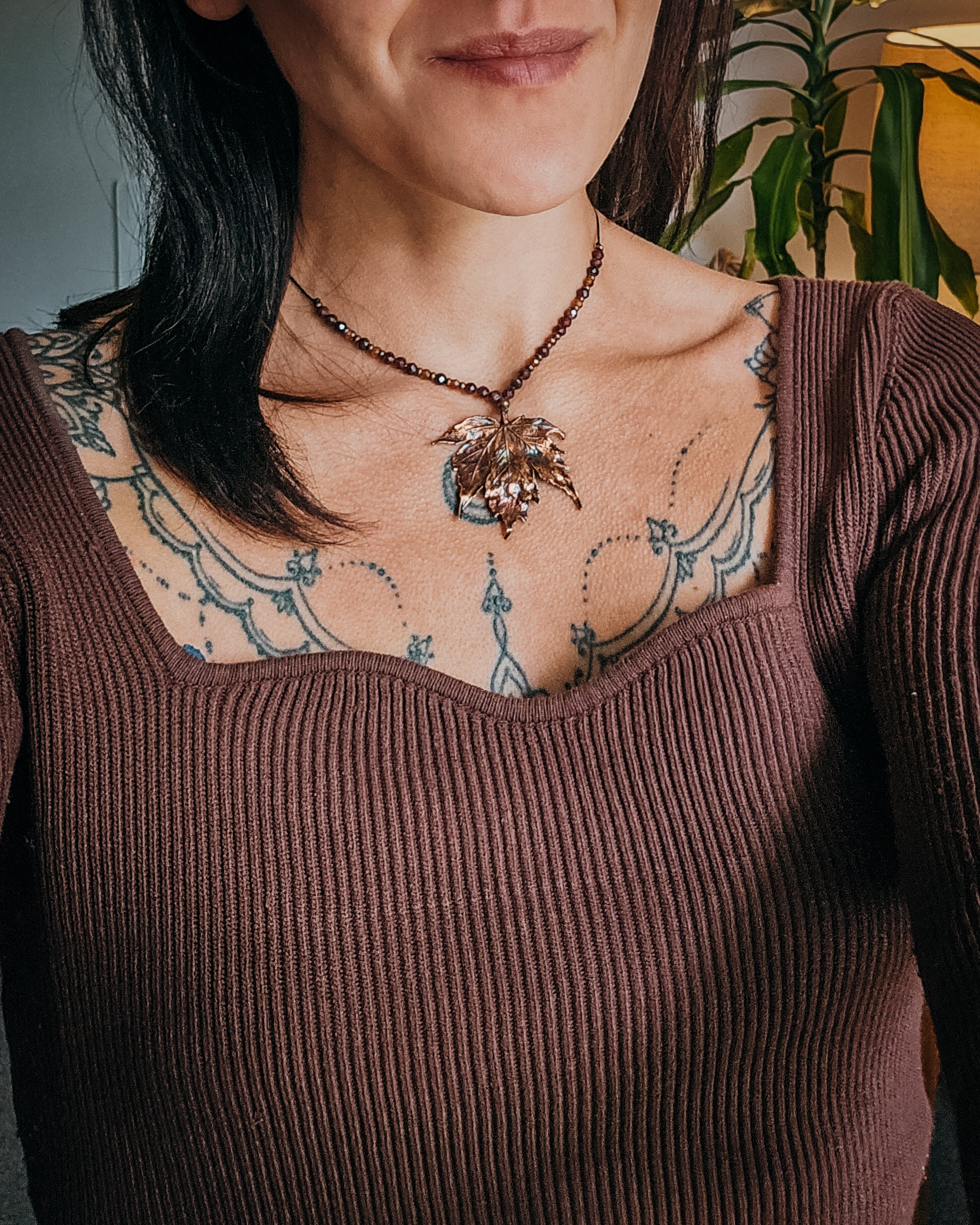 Handmade Copper electroformed Necklace with maple leaf pendant and Garnet crystal beads on a textured surface with leaves