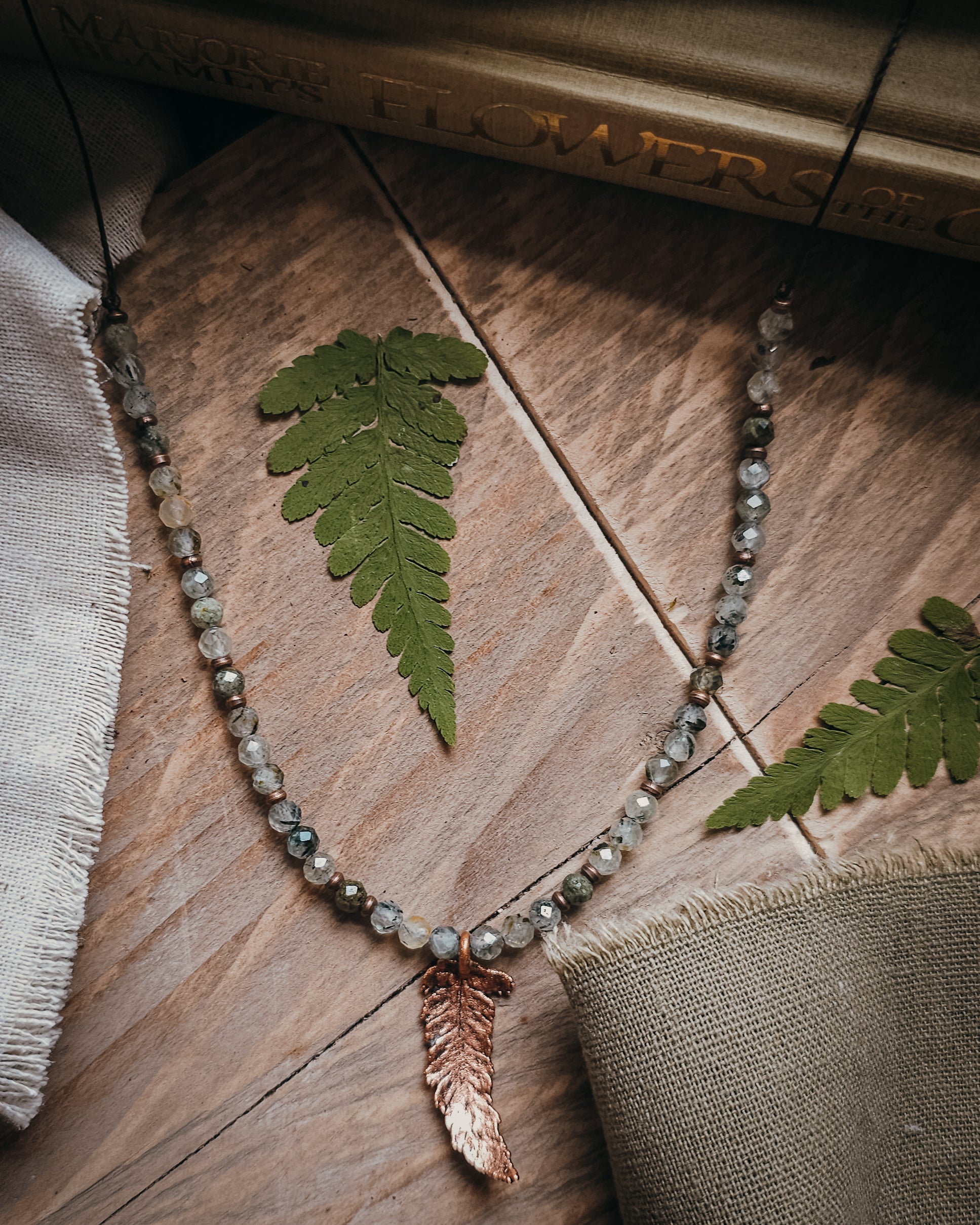 Necklace with copper electroformed fern leaf pendant and crystal Prehnite and Epidote beads on a wooden surface with fern leaves