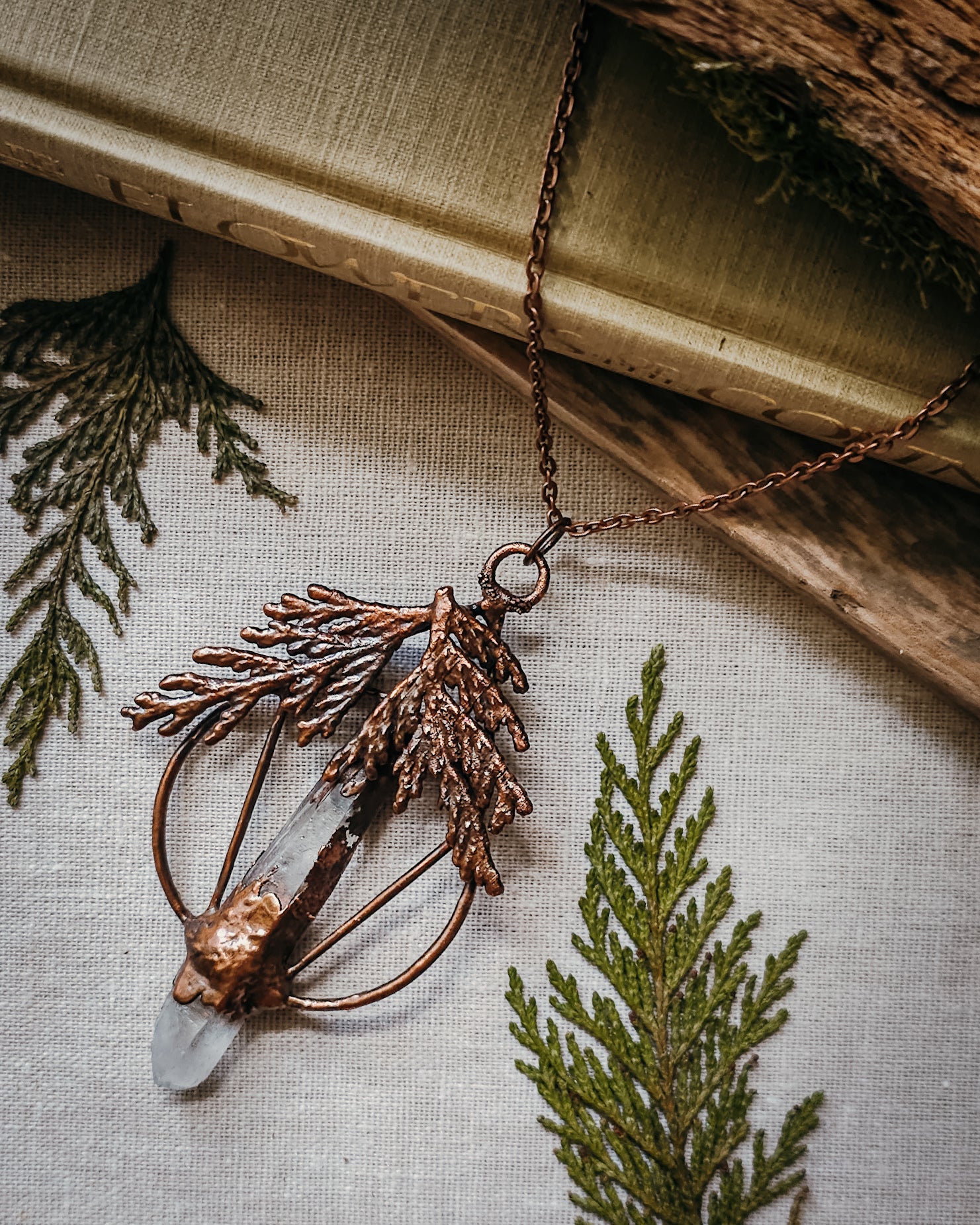 Handmade Copper electroformed Necklace with a cypress and clear Quartz crystal pendant on a textured fabric background