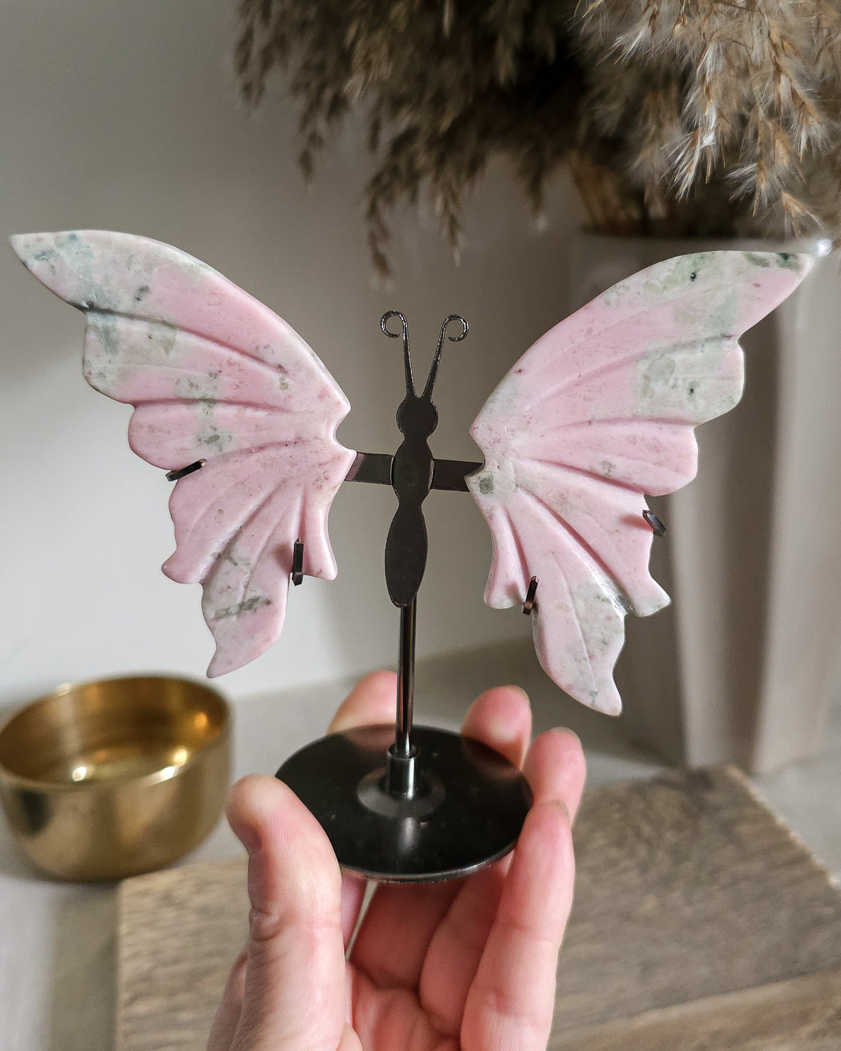Pink Opal butterfly wings carved from natural pink opal, displayed on a black metal stand, showing soft pink and creamy tones.