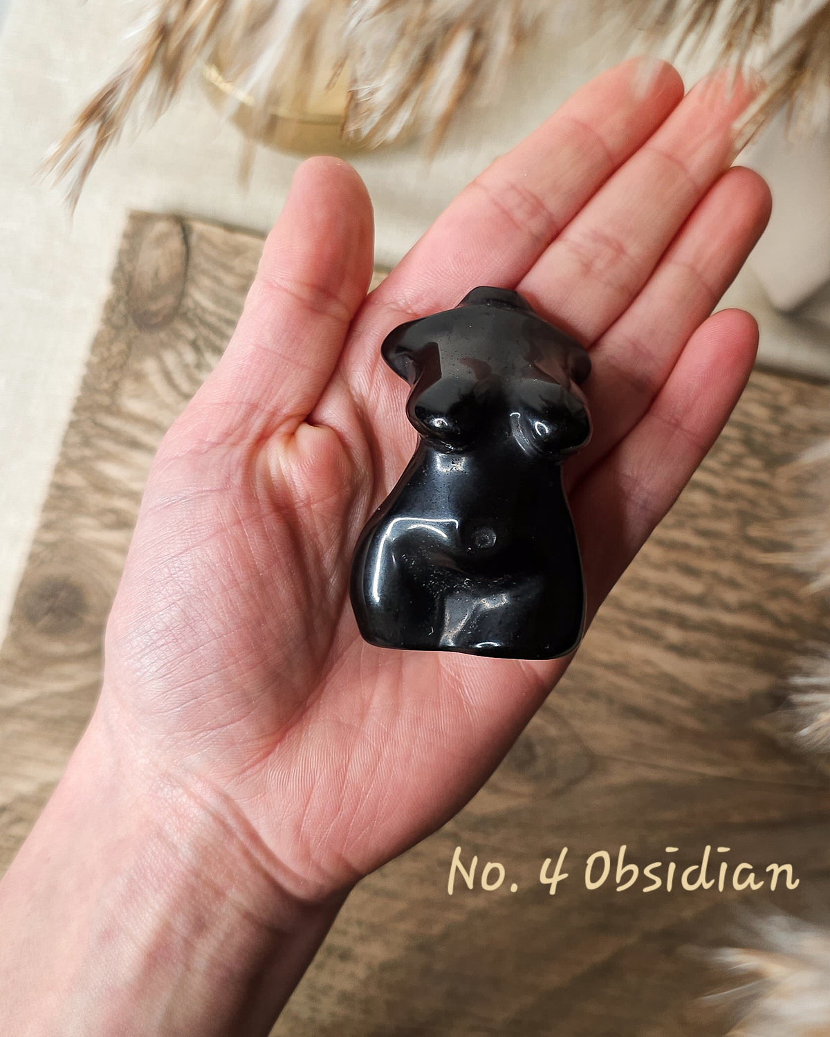 A hand holding a small polished black obsidian figurine shaped like a stylized female torso. 