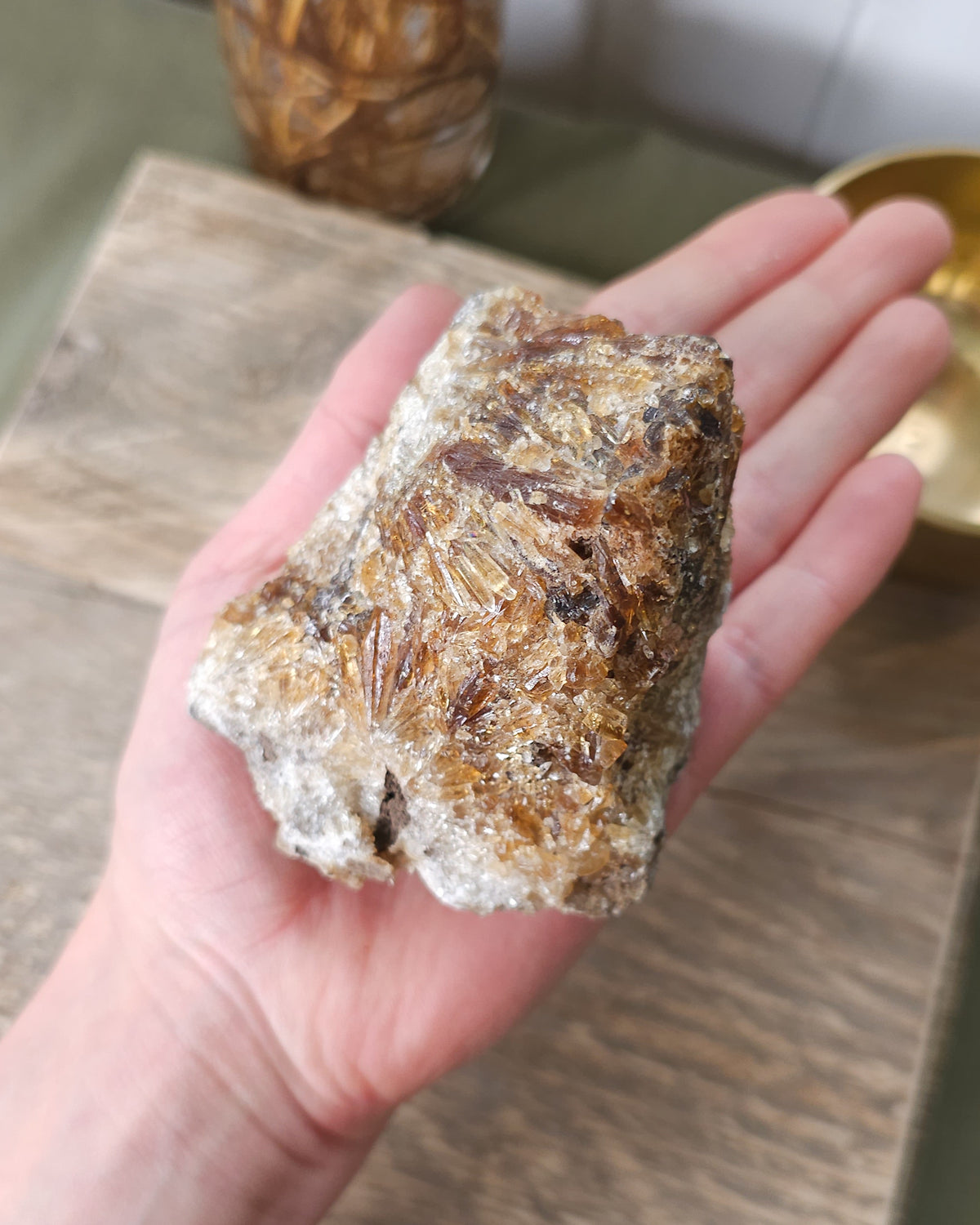 Hand holding a Mineral Amber Calcite specimen on a wooden surface with a blurred indoor background