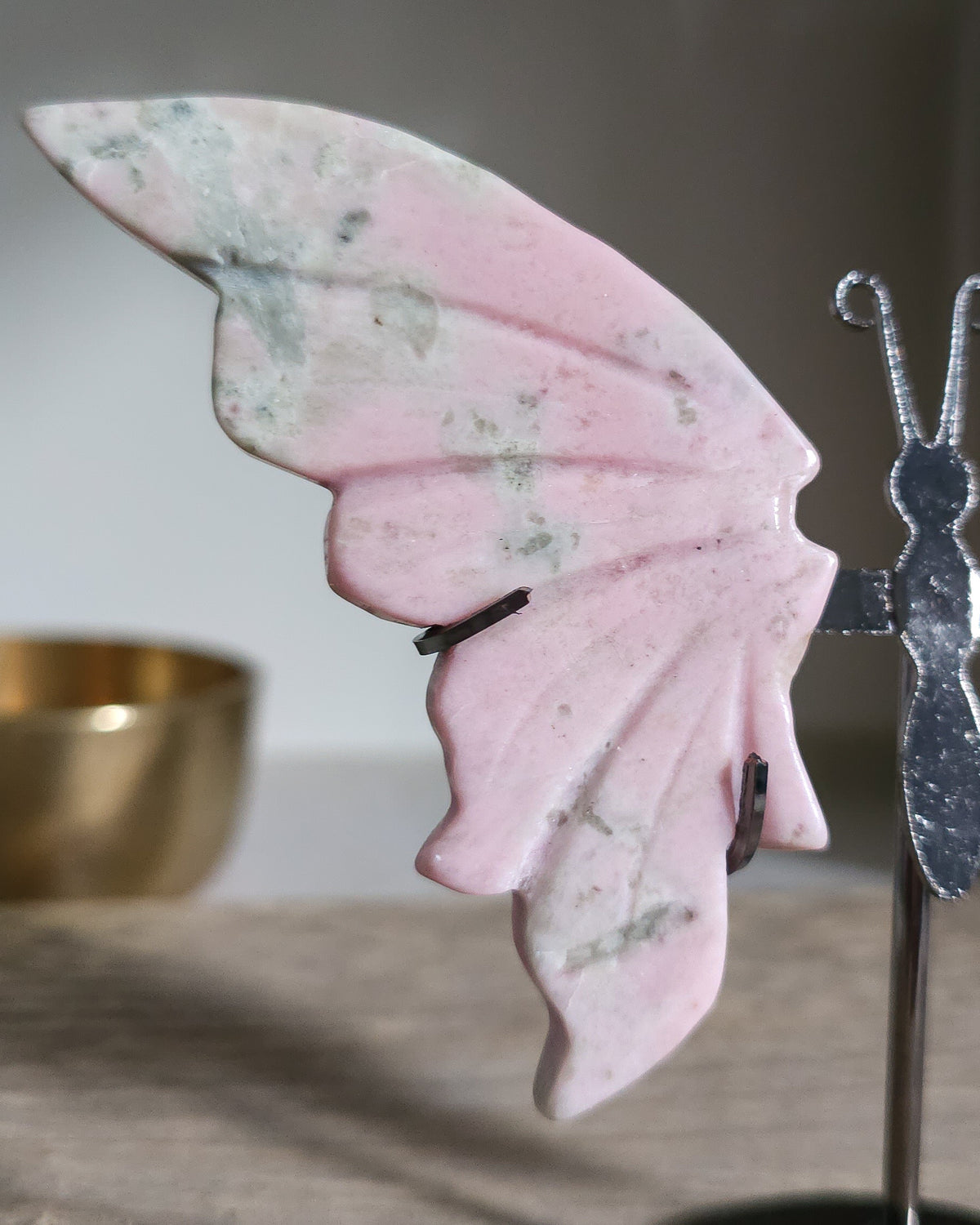 Pink Opal butterfly wings carved from natural pink opal, displayed on a black metal stand, showing soft pink and creamy tones.