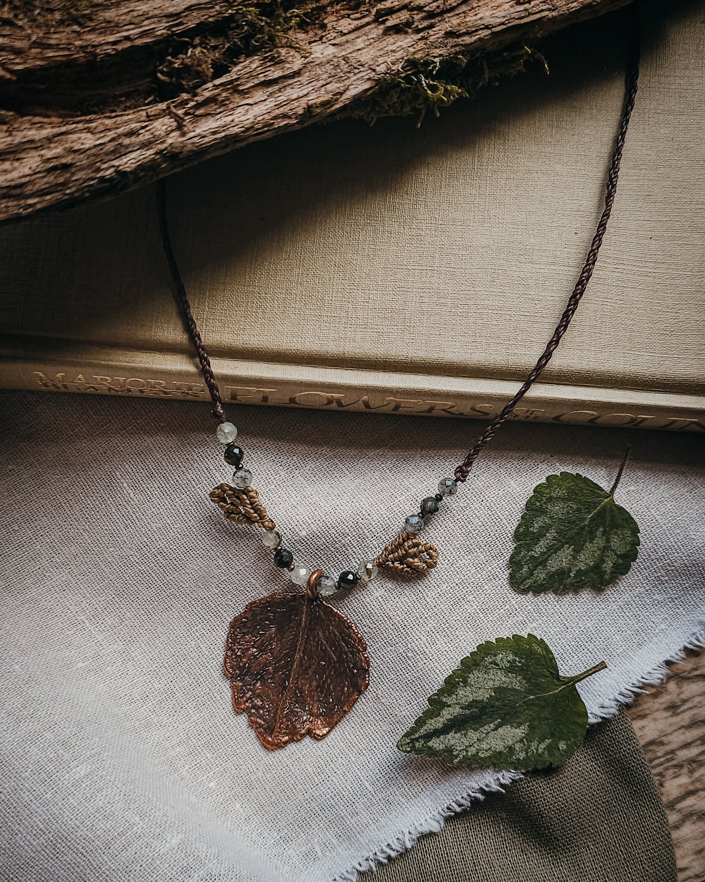 Side view of copper electroformed dead nettle leaf pendant with Prehnite and Epidote beads on a braided adjustable cord.