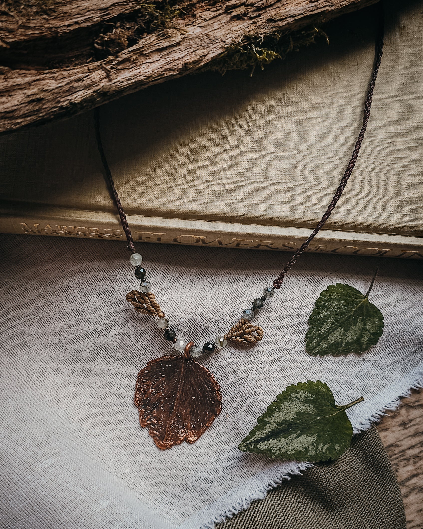 Side view of copper electroformed dead nettle leaf pendant with Prehnite and Epidote beads on a braided adjustable cord.