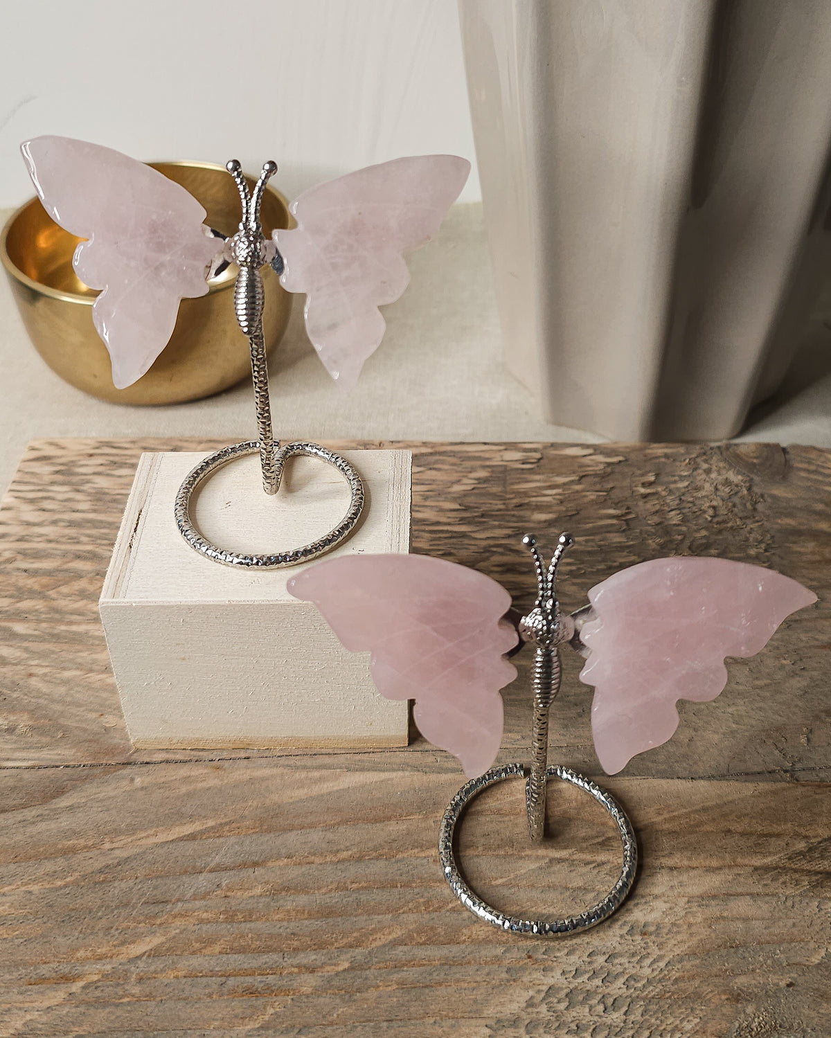 Polished rose quartz crystal butterfly carving with soft pink wings on a silver-tone display stand
