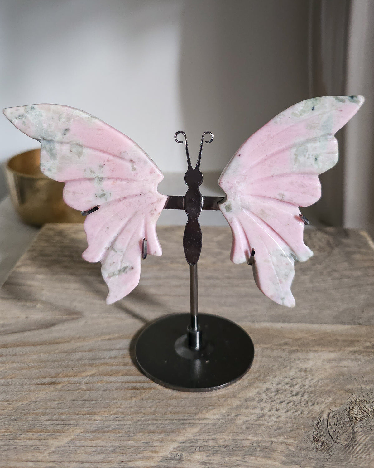 Pink Opal butterfly wings carved from natural pink opal, displayed on a black metal stand, showing soft pink and creamy tones.
