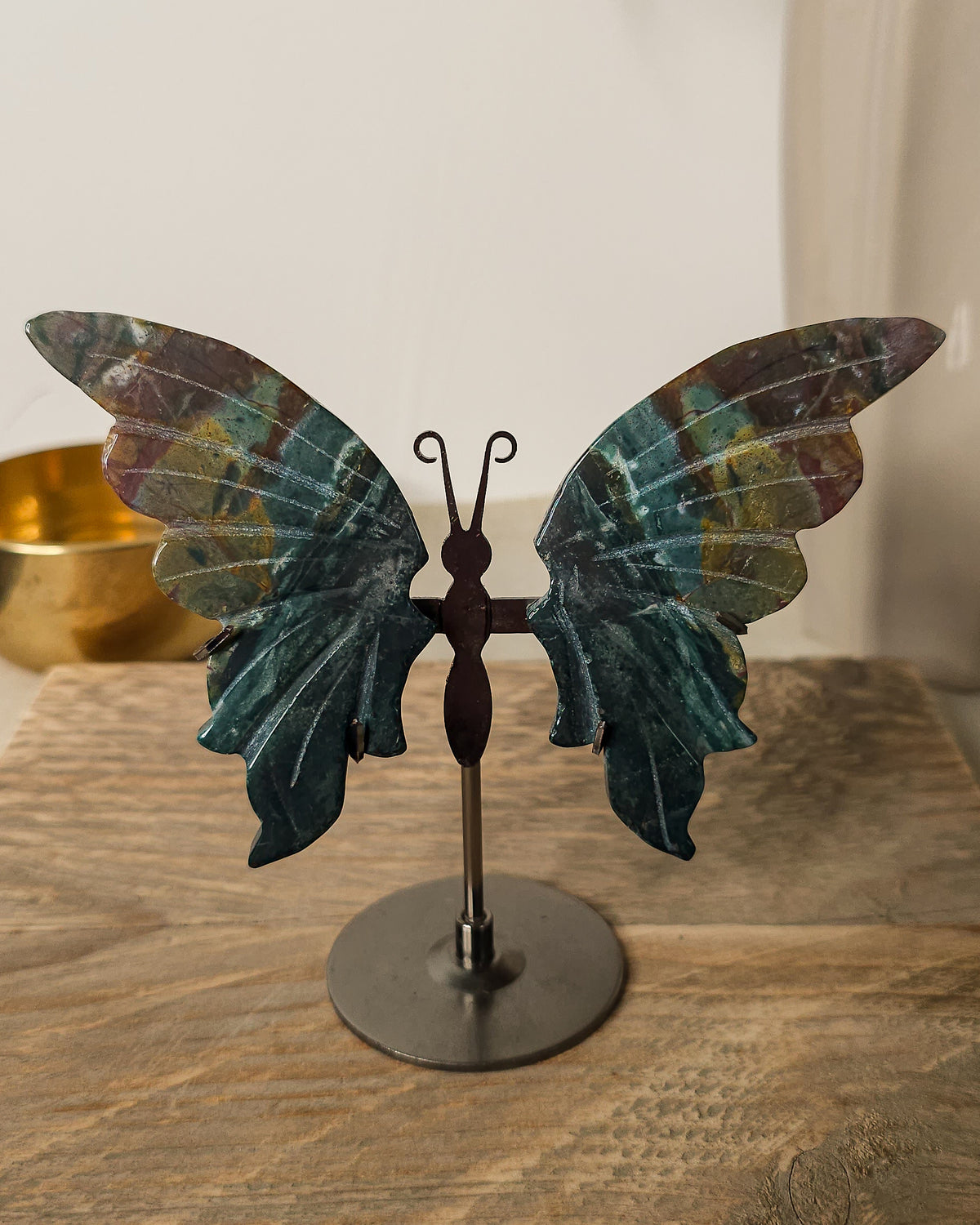 Jasper butterfly wings on a black metal stand, featuring deep green, earthy brown and golden natural patterns.. 