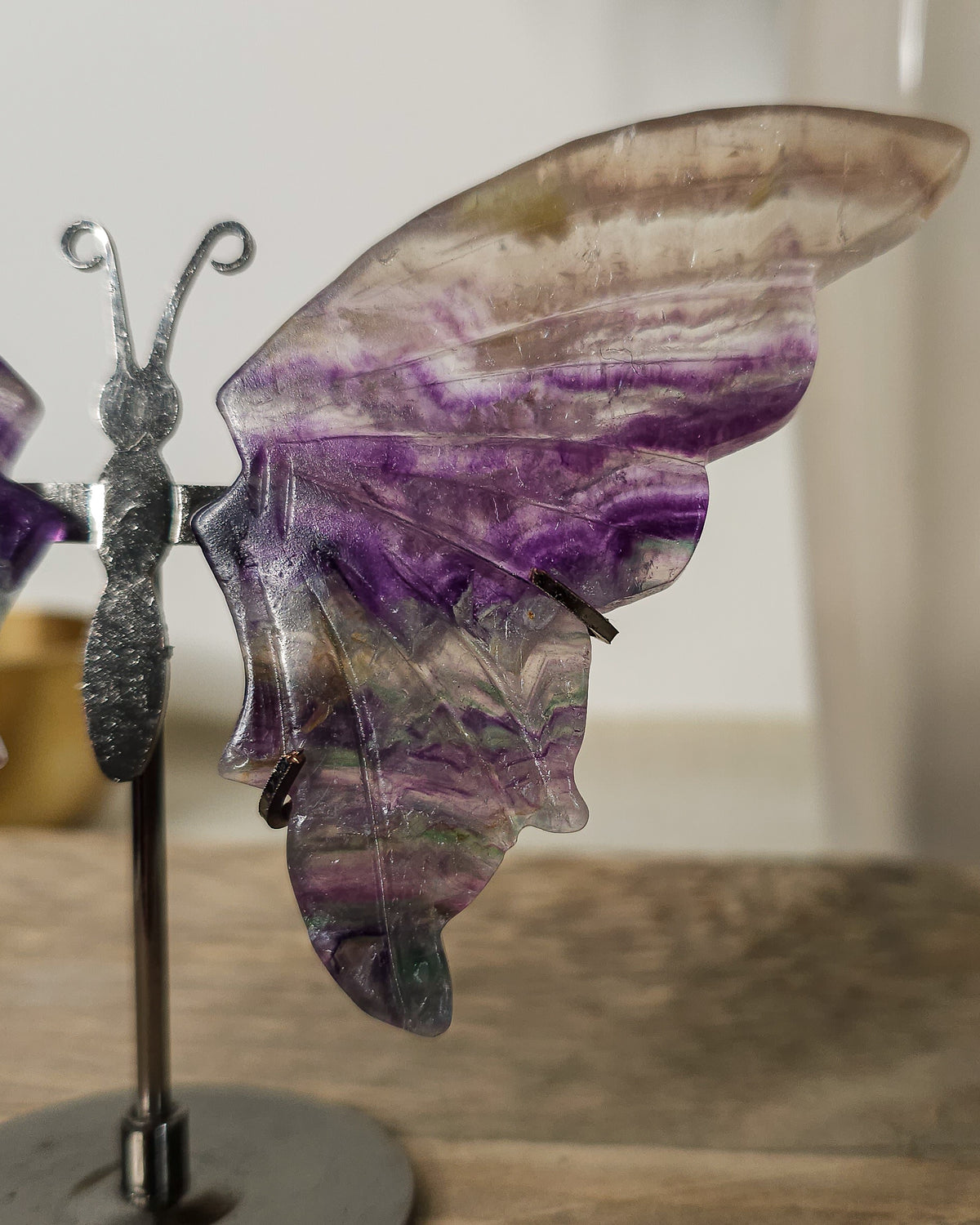 Fluorite crystal butterfly wings on a stand, with purple, green and golden tones. A beautiful display piece and meaningful gift for new beginnings.
