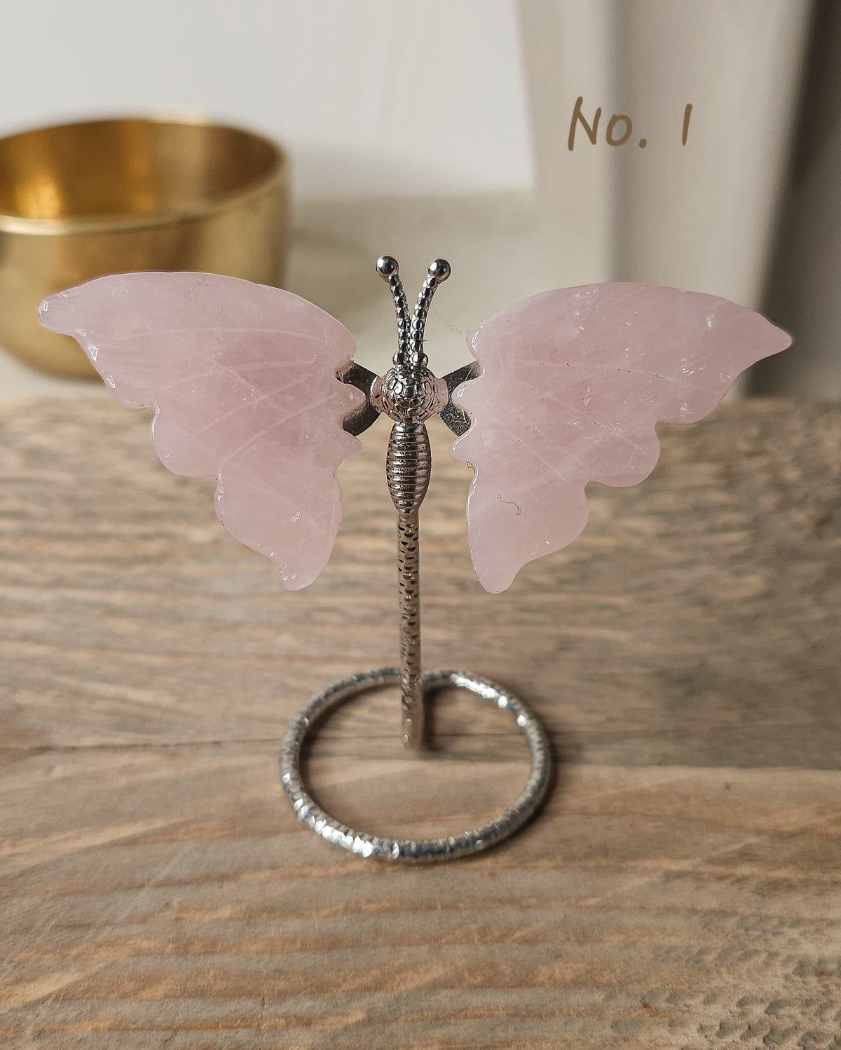 Polished rose quartz crystal butterfly carving with soft pink wings on a silver-tone display stand
