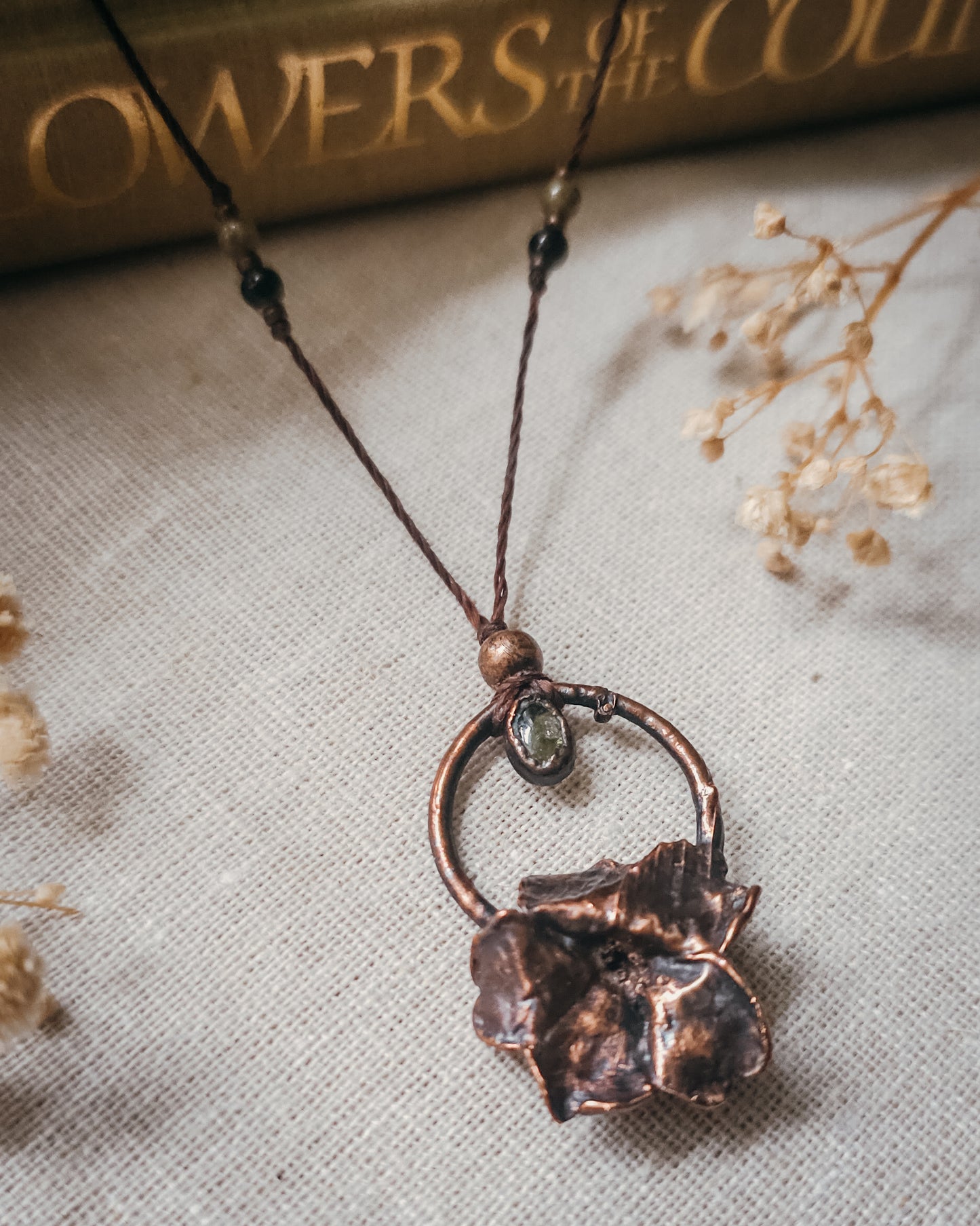 Handcrafted copper electroformed Primrose flower necklace featuring a natural Green Tourmaline stone, green and pink Tourmaline beads, brass accent beads on an adjustable cord. Created from a real Primrose flower gathered in Scotland and inspired by woodland folklore, renewal, and the magic of hidden pathways.