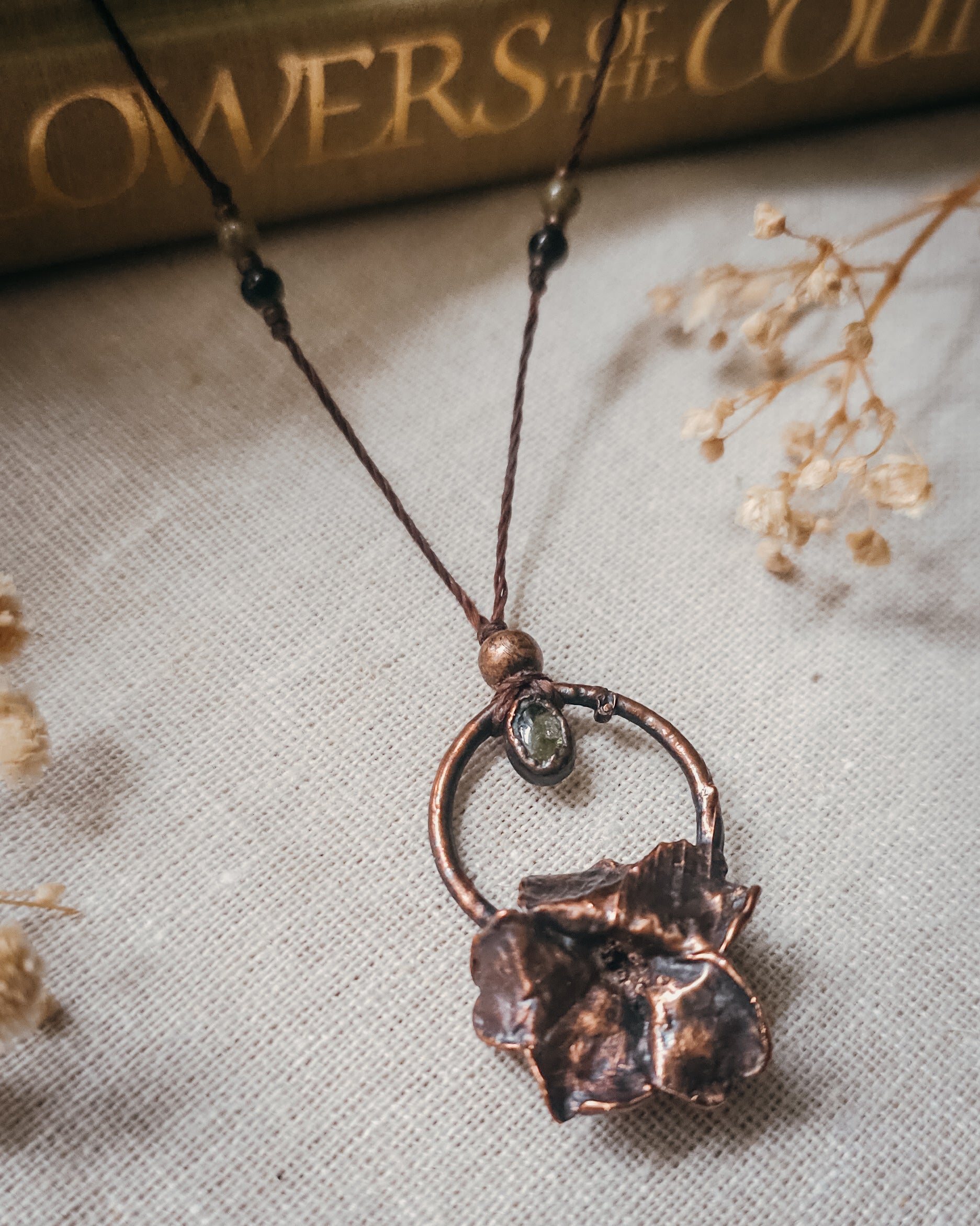 Handcrafted copper electroformed Primrose flower necklace featuring a natural Green Tourmaline stone, green and pink Tourmaline beads, brass accent beads on an adjustable cord. Created from a real Primrose flower gathered in Scotland and inspired by woodland folklore, renewal, and the magic of hidden pathways.