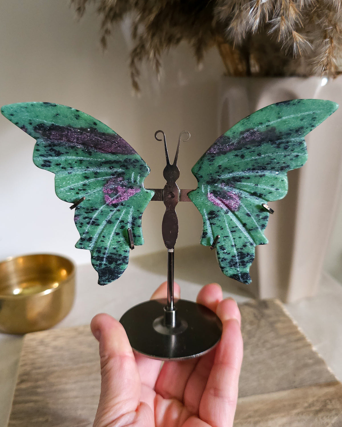 Ruby in Zoisite butterfly wings with fluorescent Ruby inclusions on a black metal stand, glowing vivid pink-red under UV light.