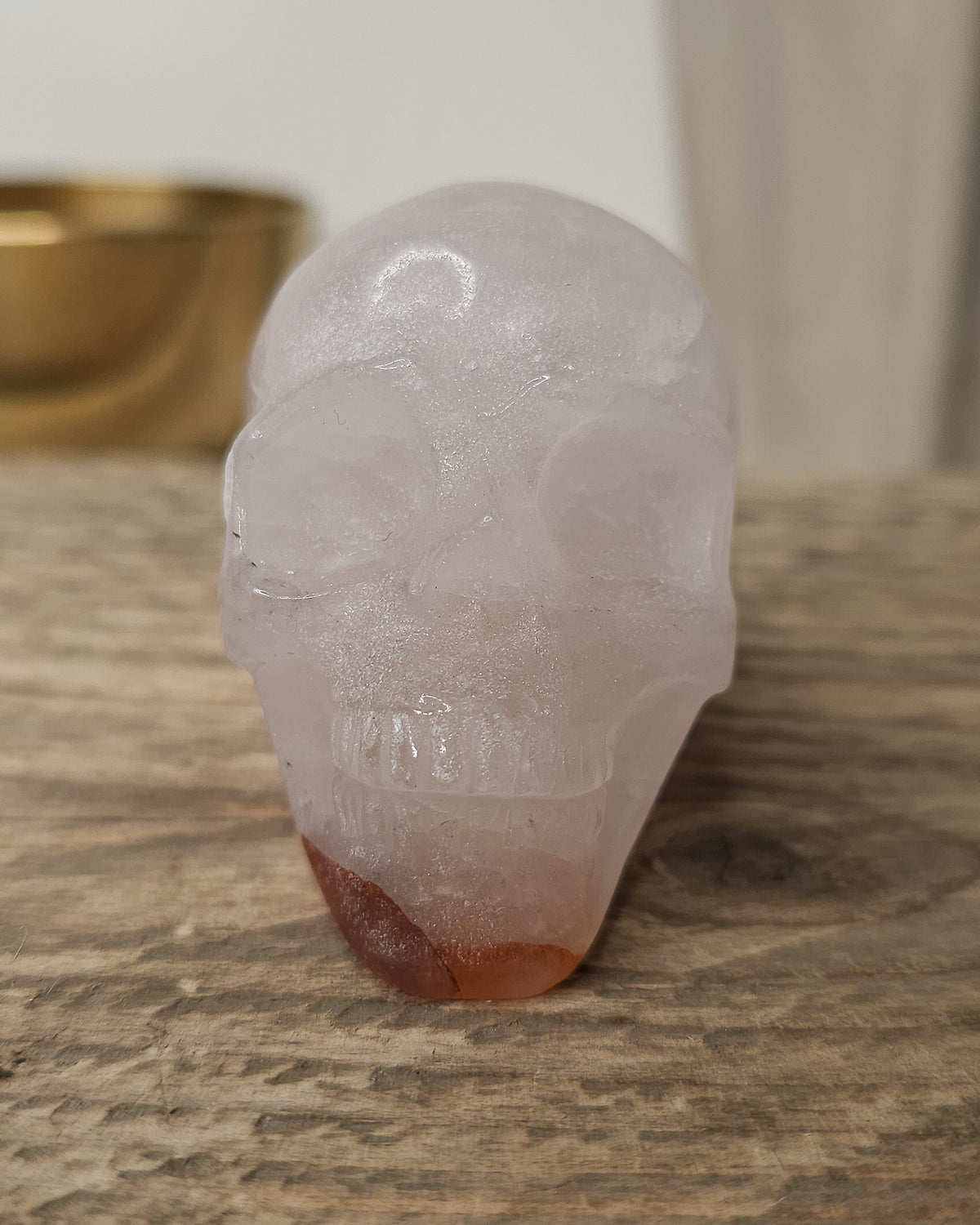 Rose Quartz crystal skull with natural red Hematite inclusions, showing soft pink tones and a reddish patch at the base.