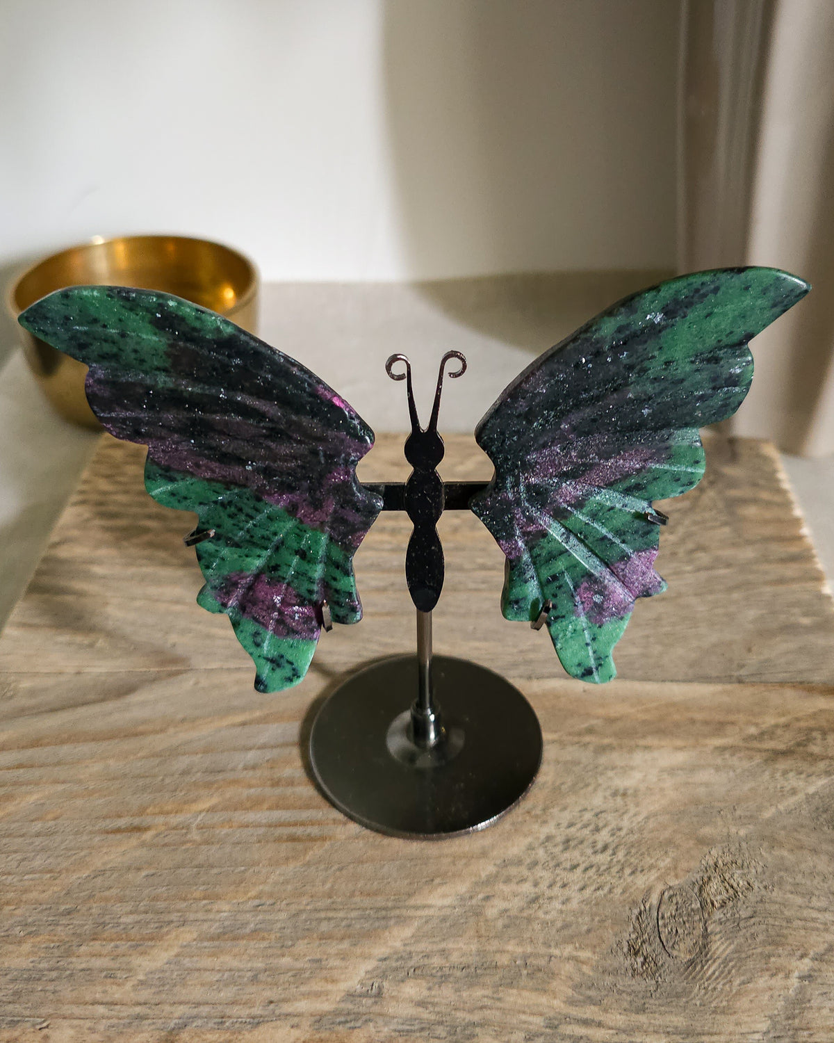Ruby in Zoisite butterfly  wings with fluorescent Ruby inclusions on a black metal stand, glowing vivid pink-red under UV light.