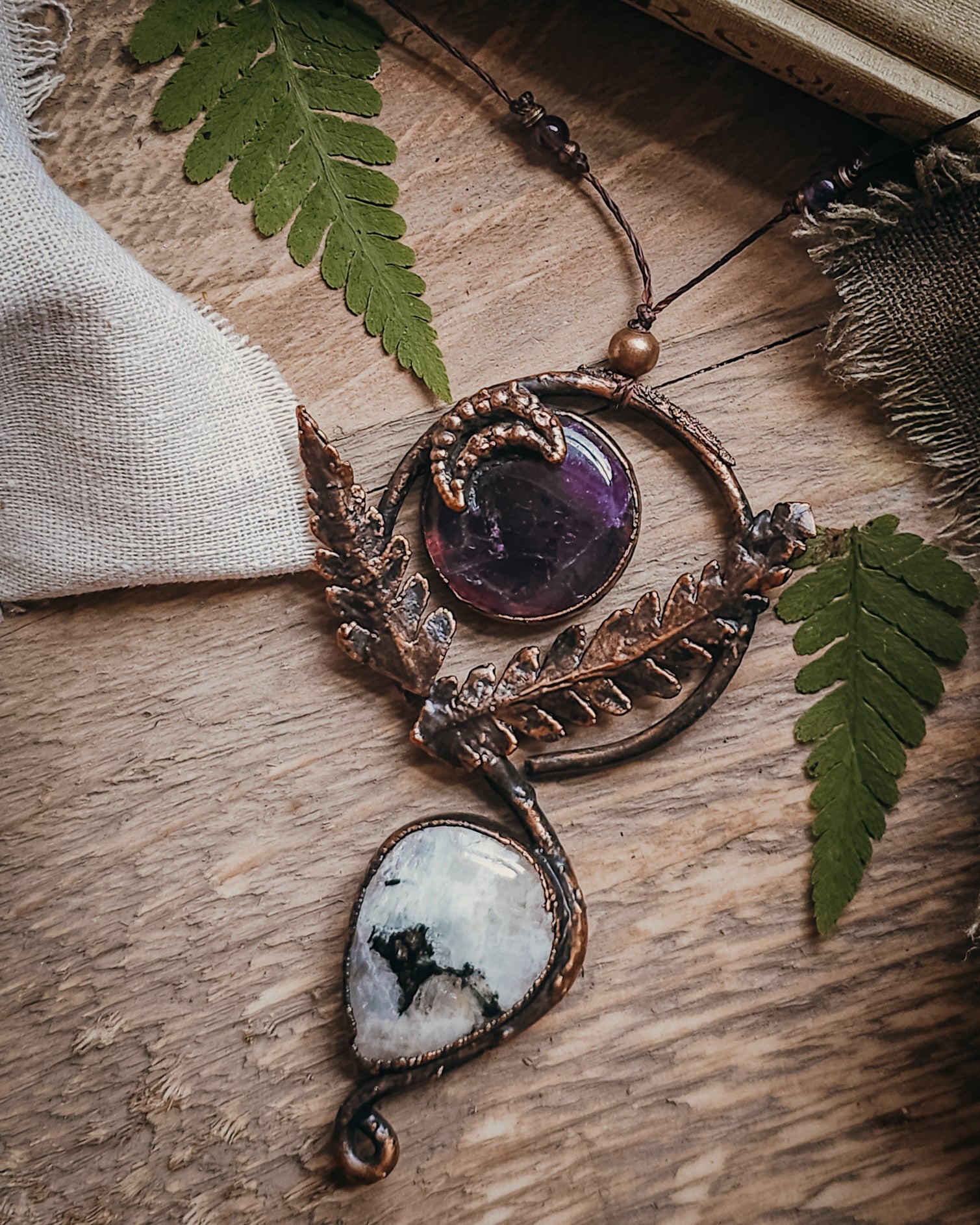 Copper electroformed Ornate pendant with amehtyst, Moonstone and fern leaves on a wooden surface with leaves