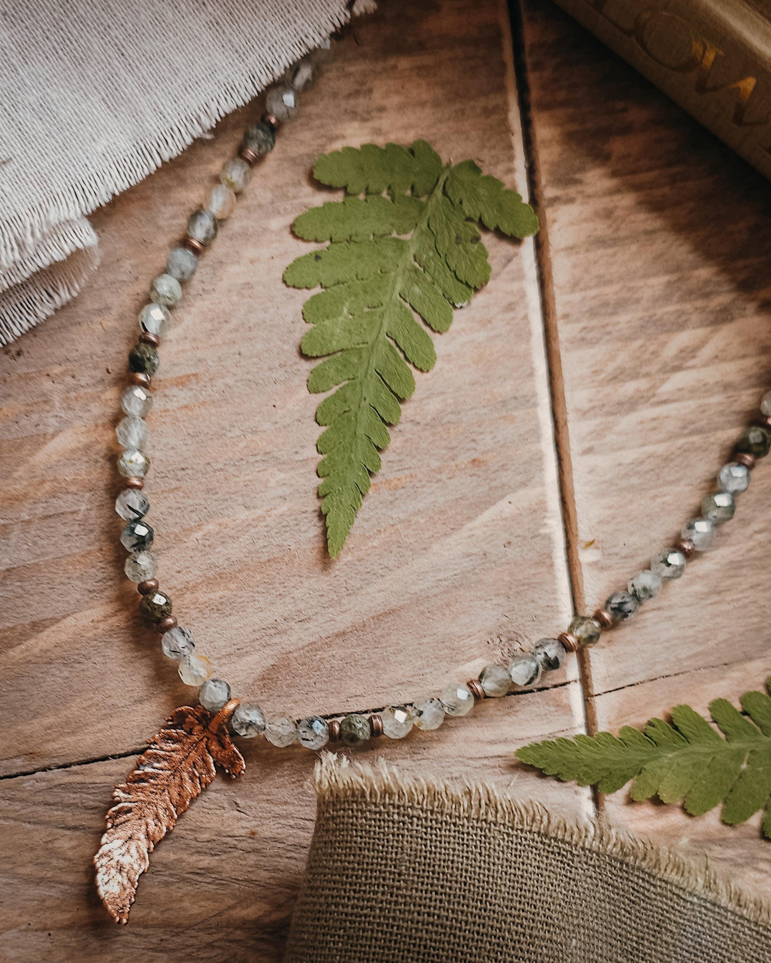 Necklace with copper electroformed fern leaf pendant and crystal Prehnite and Epidote beads on a wooden surface with fern leaves
